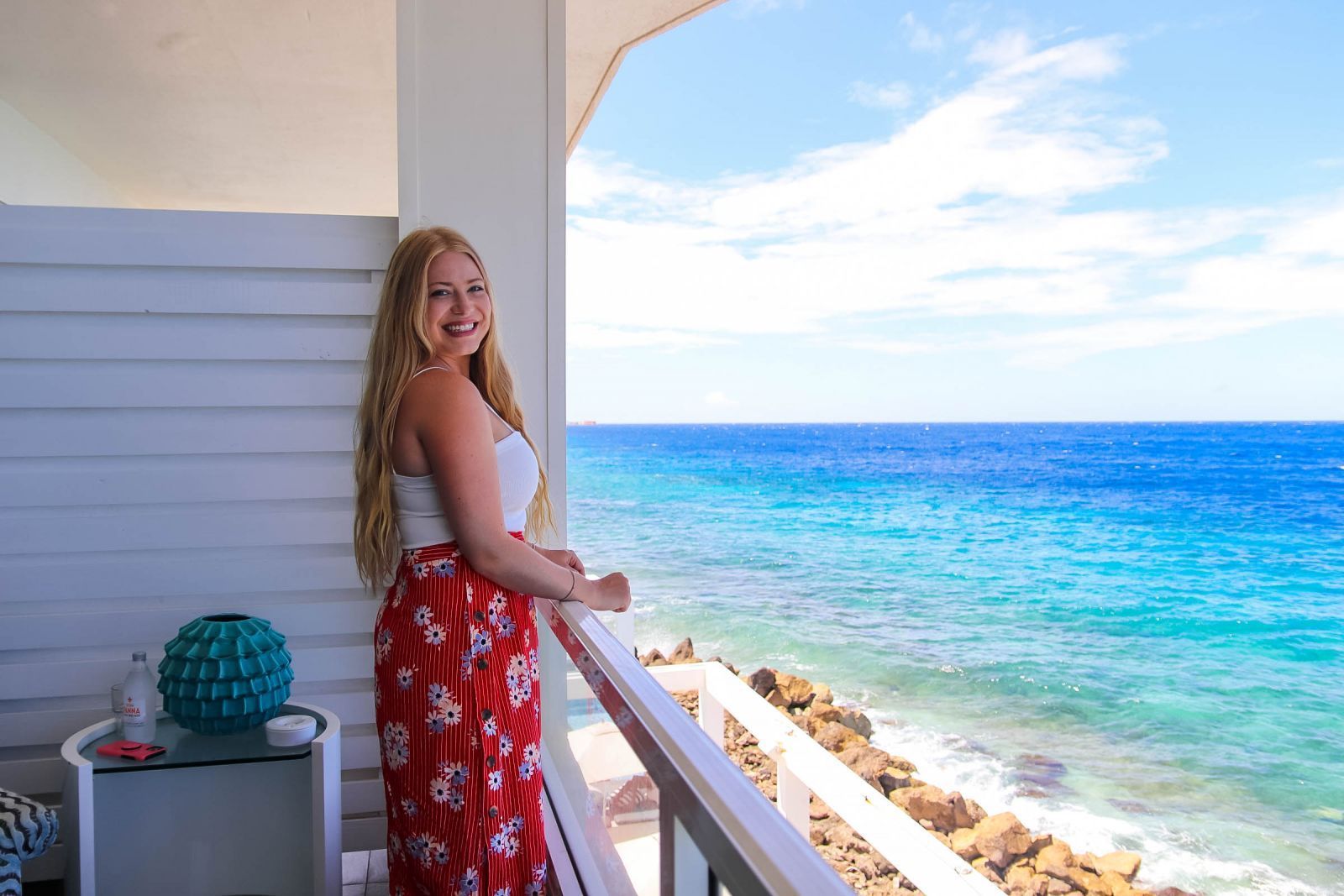 A woman is standing on a balcony overlooking the ocean.