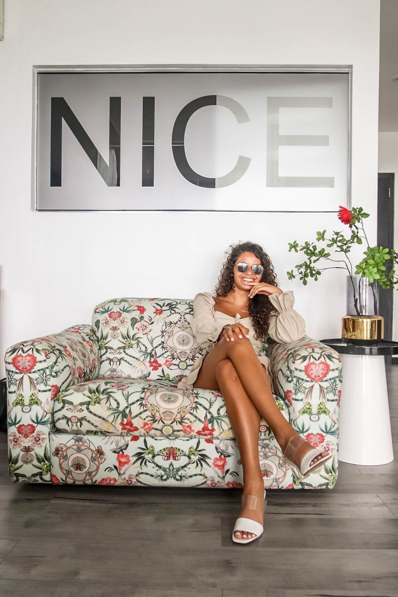 A woman is sitting on a couch in front of a sign that says nice.