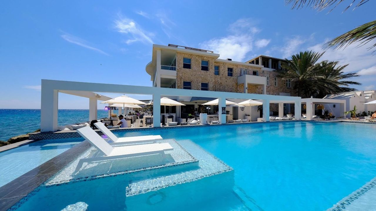 A large swimming pool surrounded by chairs and umbrellas with a building in the background.
