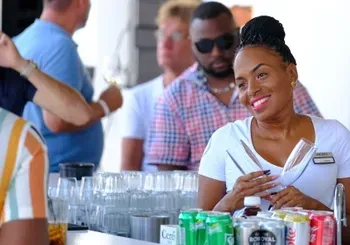 A woman is smiling while sitting at a bar surrounded by cans of soda.