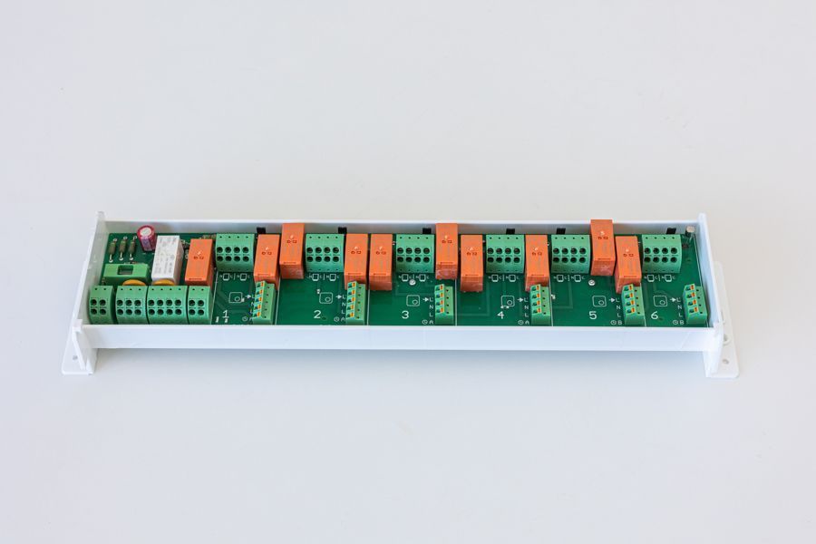 Eine grün-weiße elektronische Platine mit orangefarbenen Relais auf einer weißen Oberfläche.