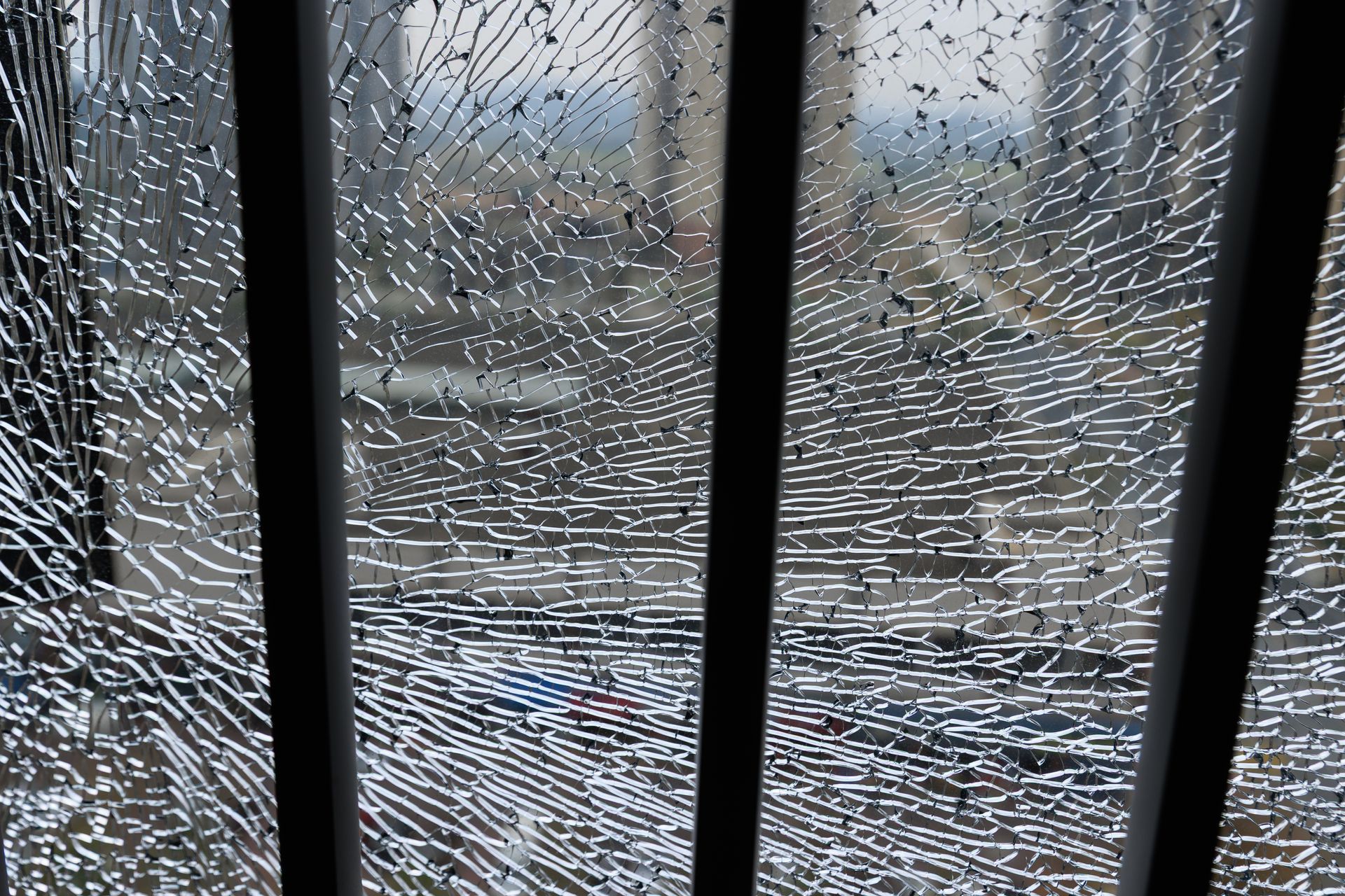 Vue d'une rue de la ville à travers une grande vitre brisée encadrée de barreaux sombres.
