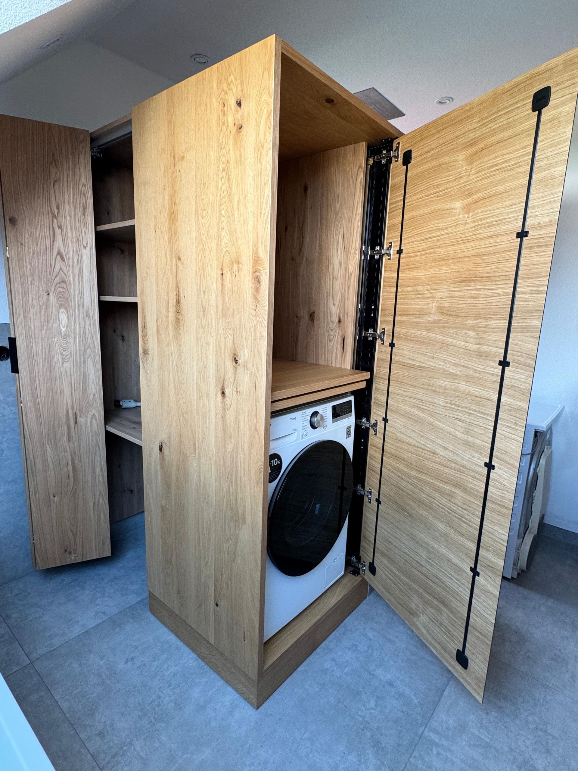 Offener Wäscheschrank aus Holz mit einer Waschmaschine im Inneren und Regalen auf der linken Seite