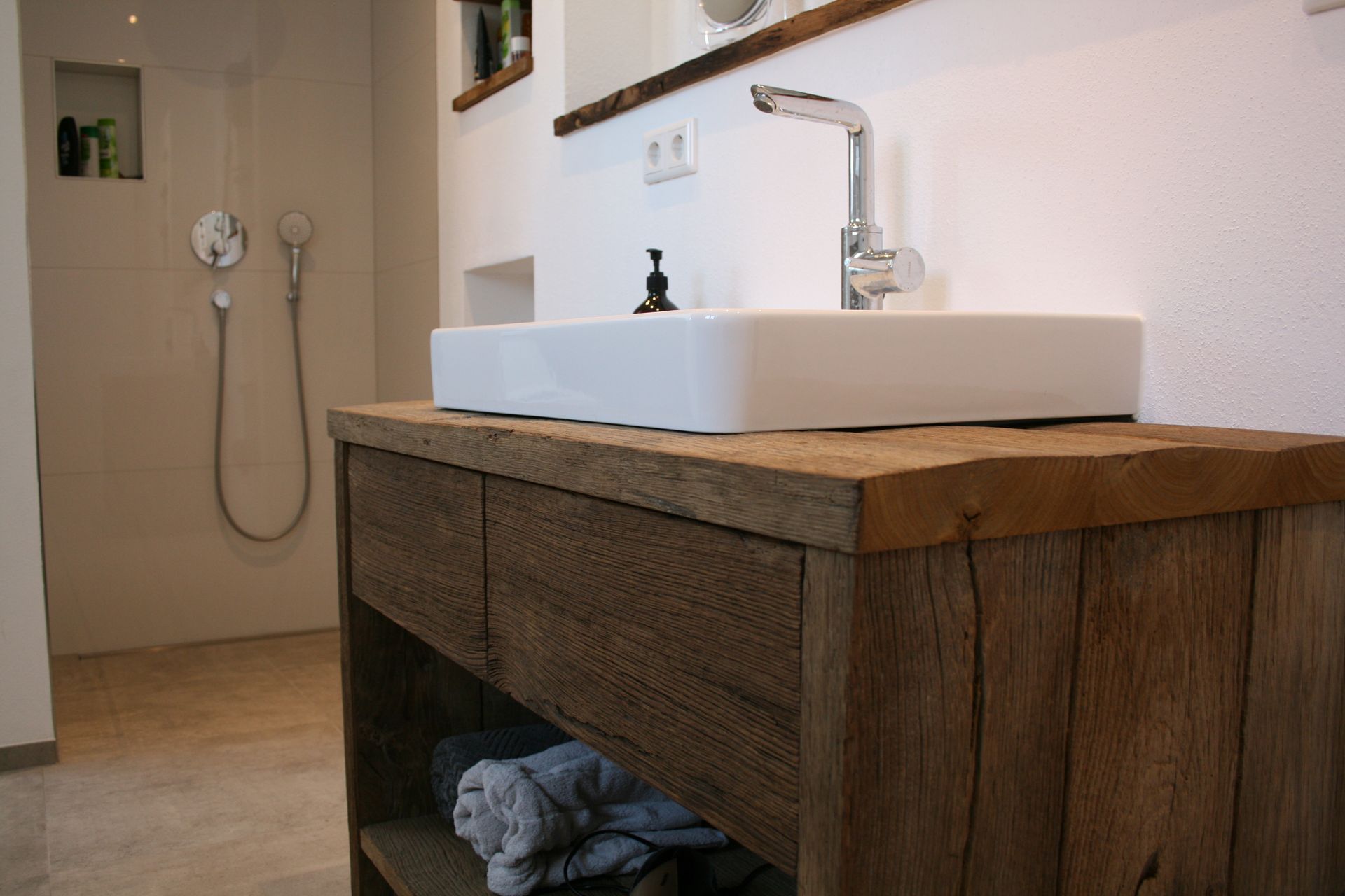 Rustikales Badezimmer mit weißem Waschbecken auf einem Waschtisch aus Holz und einer wandmontierten Duscharmatur.