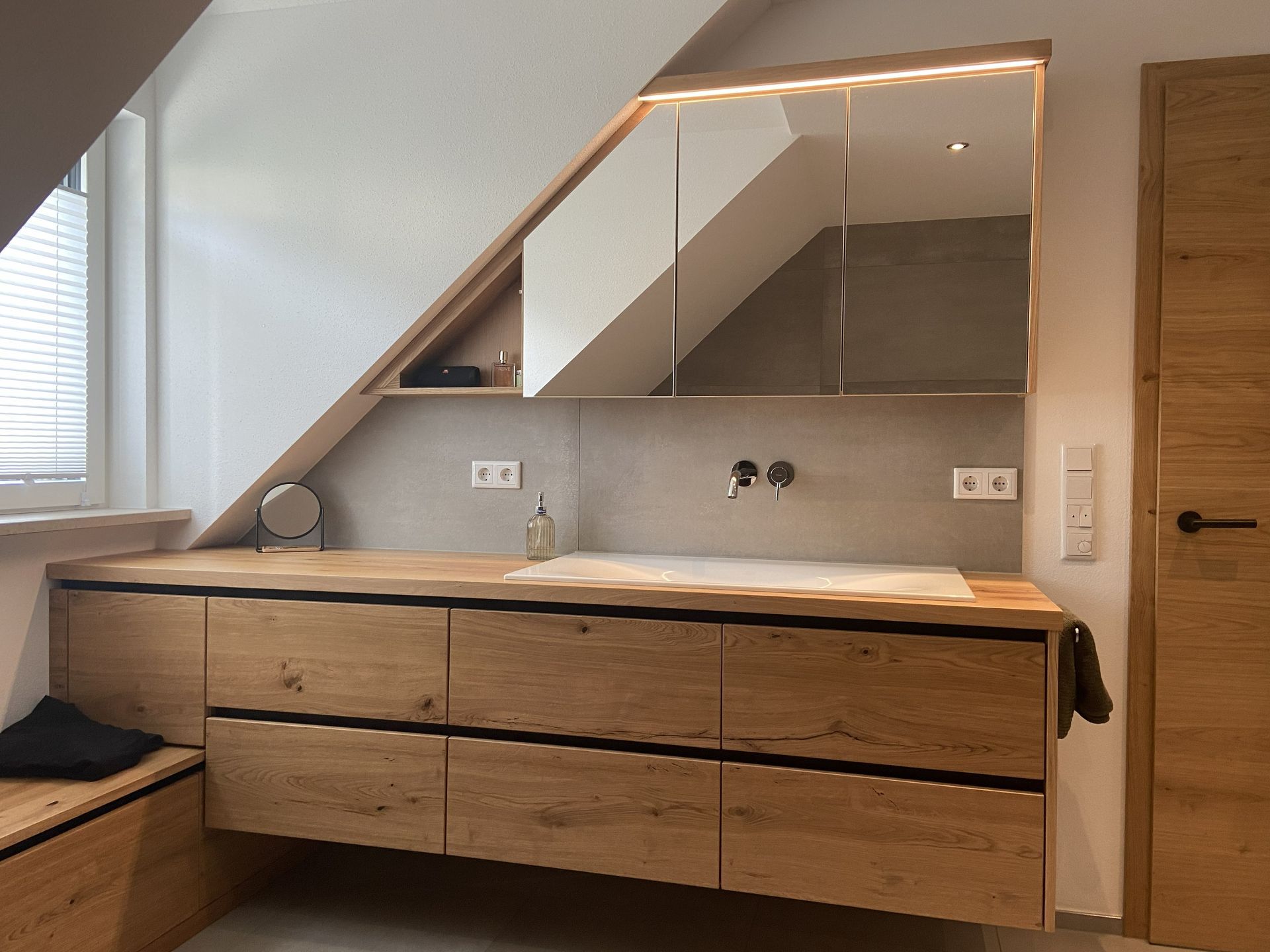 Modernes Badezimmer-Waschtischensemble mit Holzschränken, großem Spiegel, Waschbecken und Oberlicht unter einer Dachschräge