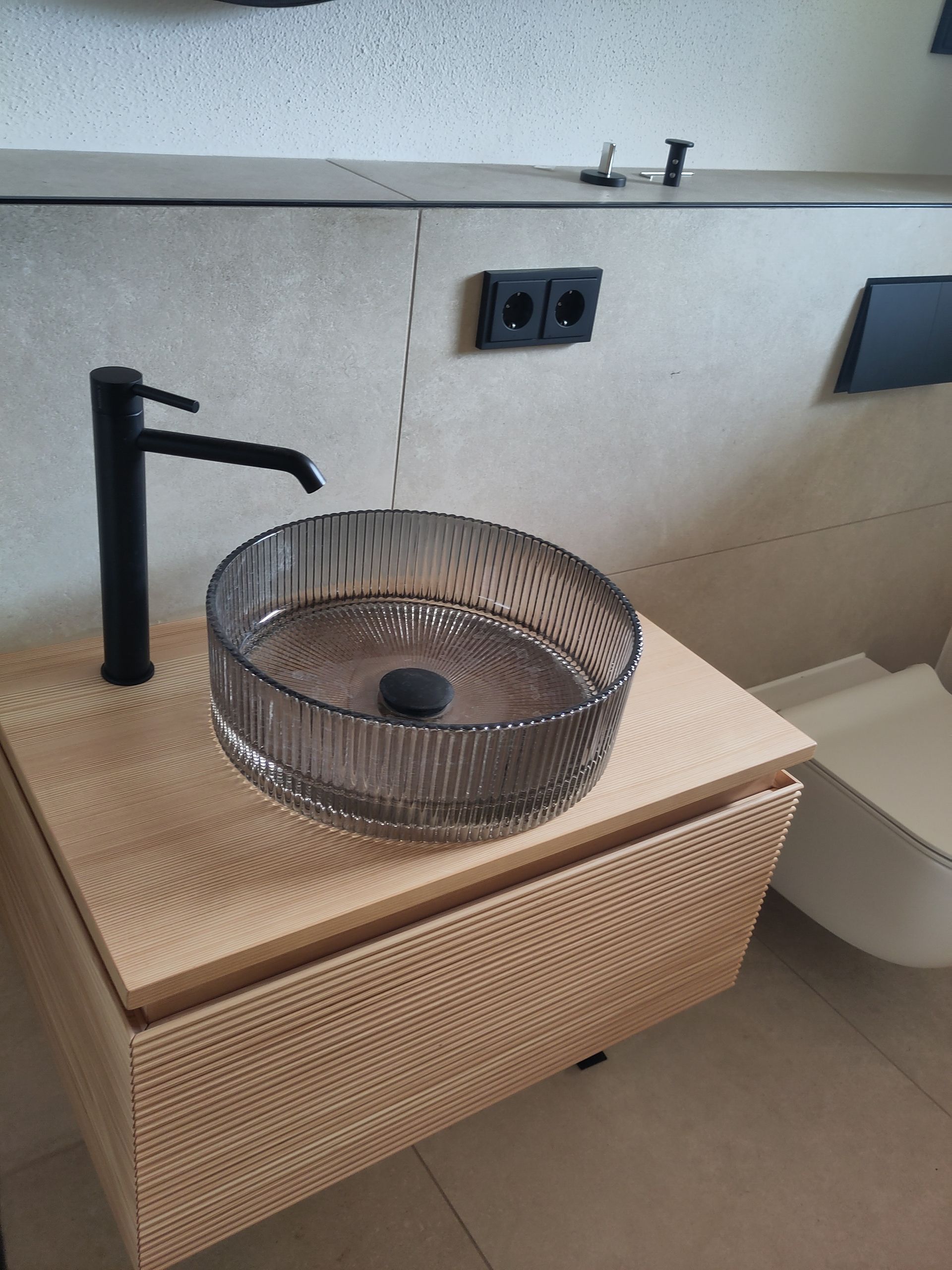 Moderner Waschtisch mit schwarzer Armatur, geflochtenem Aufsatzwaschbecken und beigefarbenem Unterschrank.