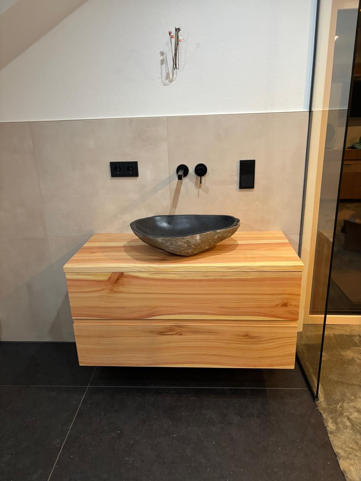 Moderner Waschtisch fürs Bad mit Holzschrank und schwarzem Aufsatzwaschbecken vor einer gefliesten Wand