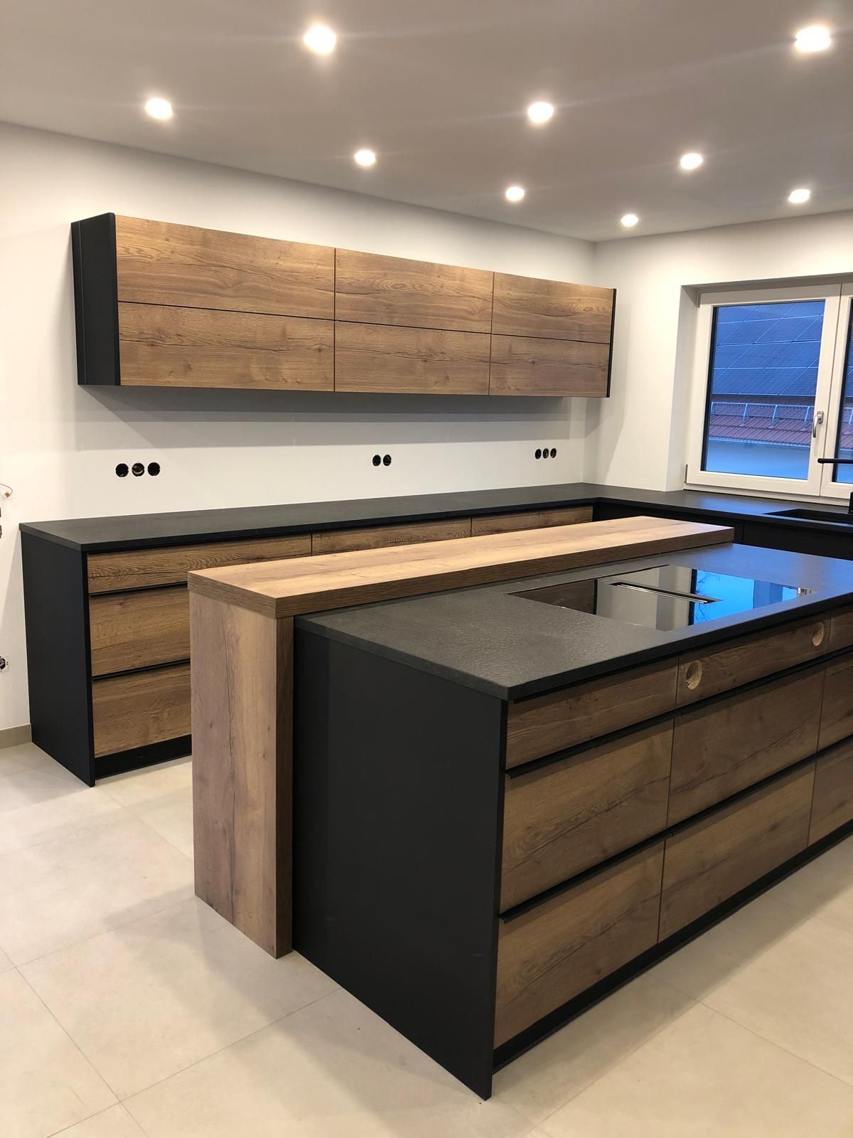 Moderne Küche mit Holzschränken, schwarzer Kochinsel und weißen Wänden unter Einbaudeckenleuchten