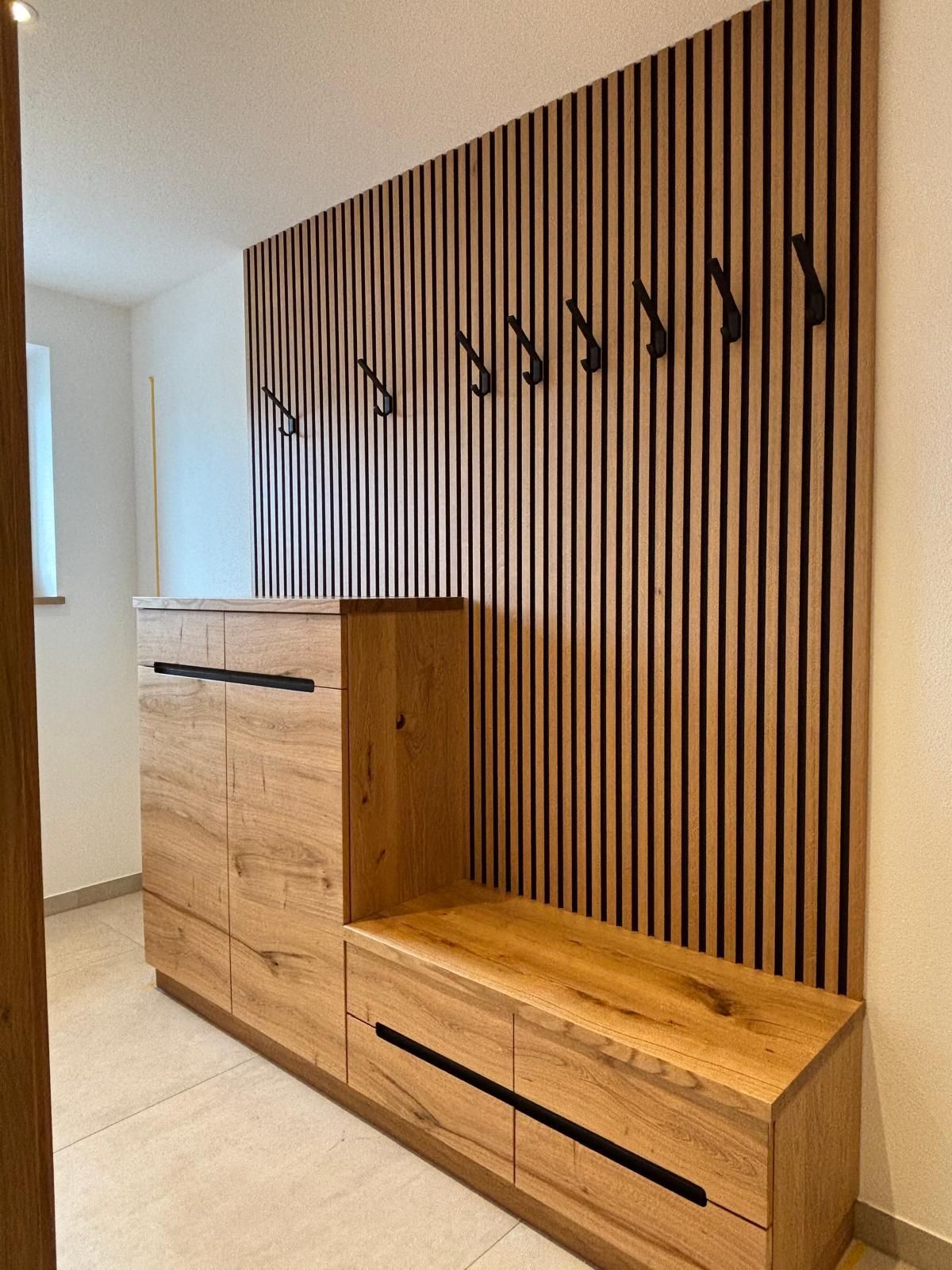 Moderner Flur mit einer Sitzbank aus Eichenholz mit Stauraum, Schubladen und einer Wandgarderobe mit vertikalen Holzlatten