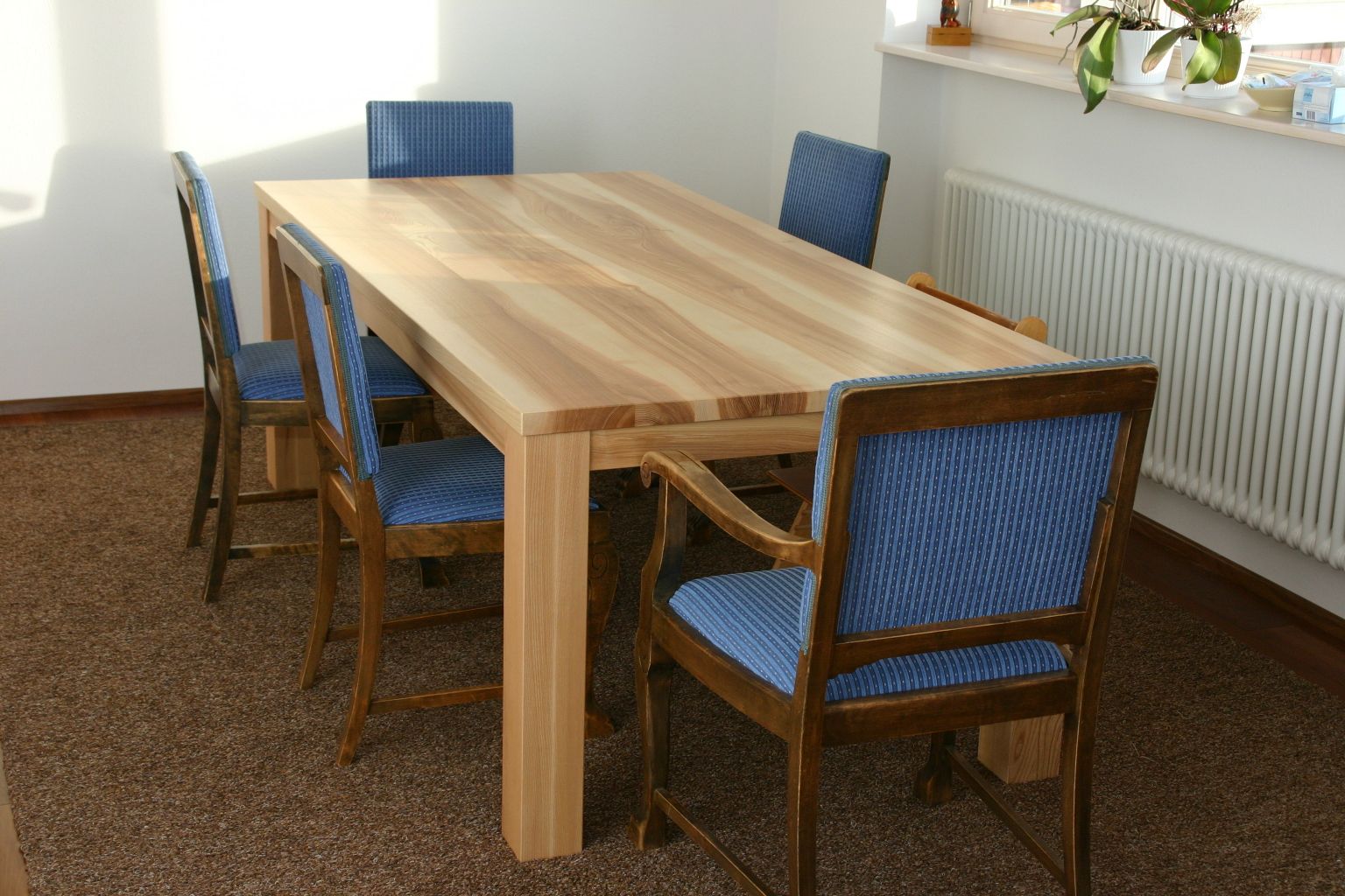Holzesstisch mit vier blau gepolsterten Stühlen in einem hellen Raum.