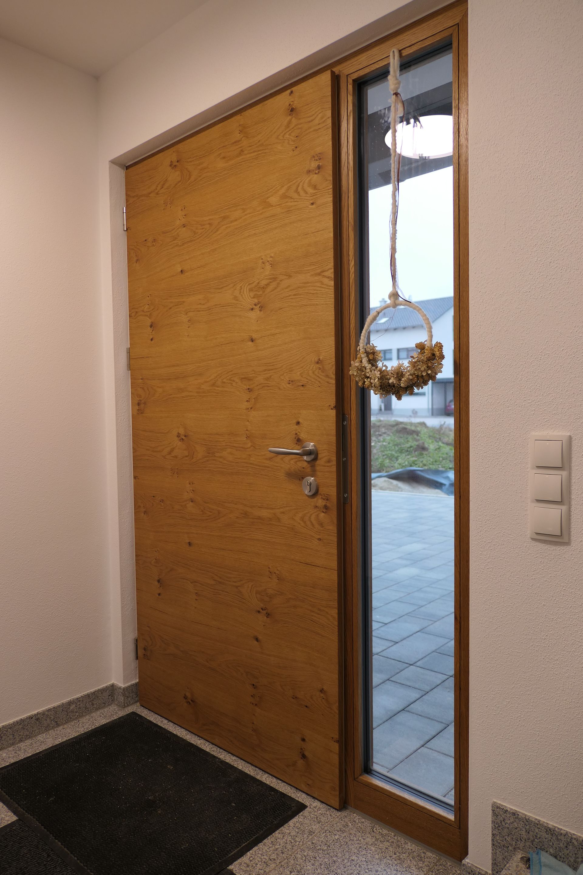 Holzhaustür mit schmalem Glaseinsatz und Kranz, von innen betrachtet.