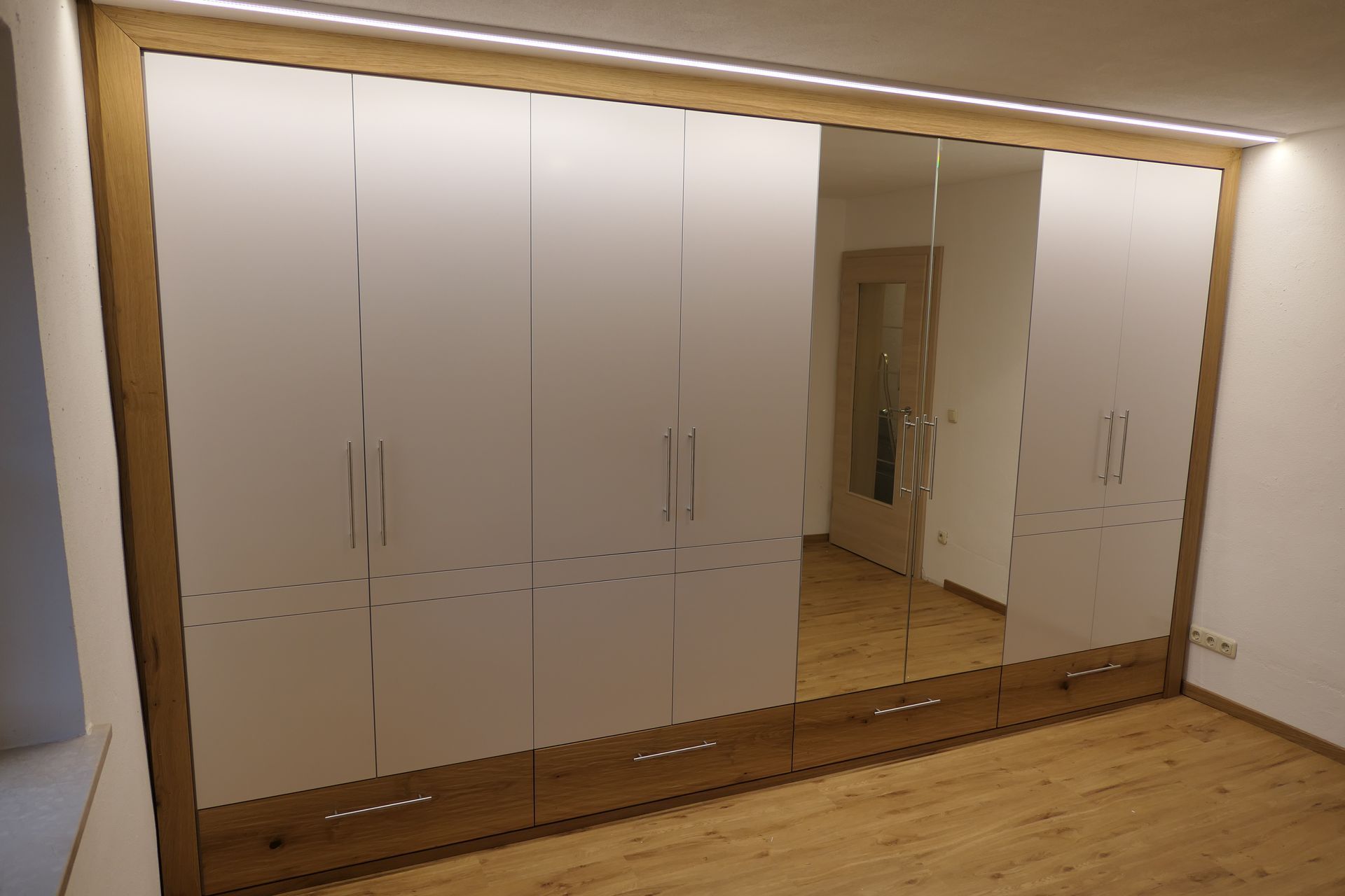 Einbauschränke in Weiß mit einer großen Spiegeltür in einem Schlafzimmer mit Holzboden