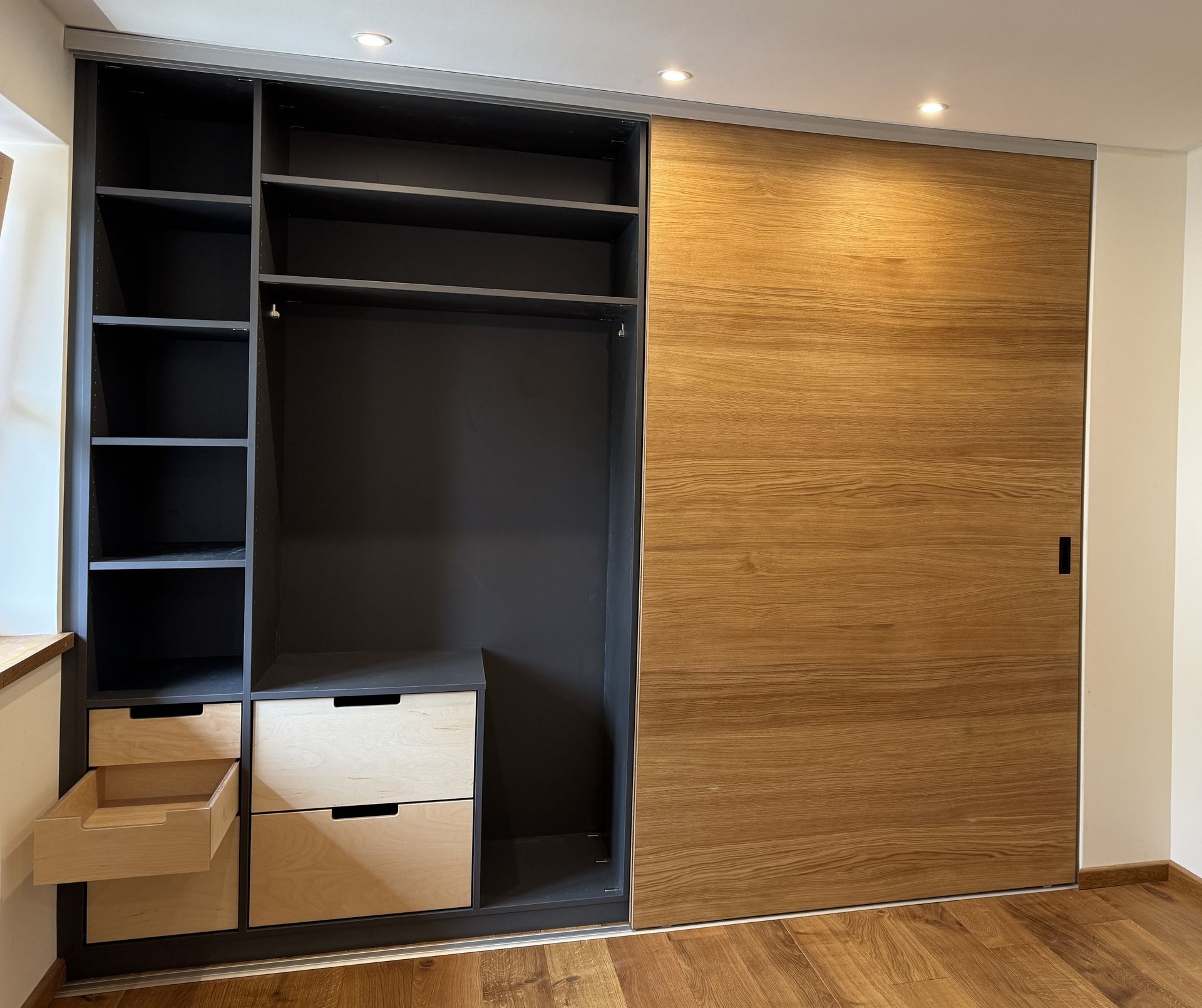 Offener Kleiderschrank mit schwarzen Regalböden und einer Kleiderstange neben einer großen Schiebetür aus Holz.
