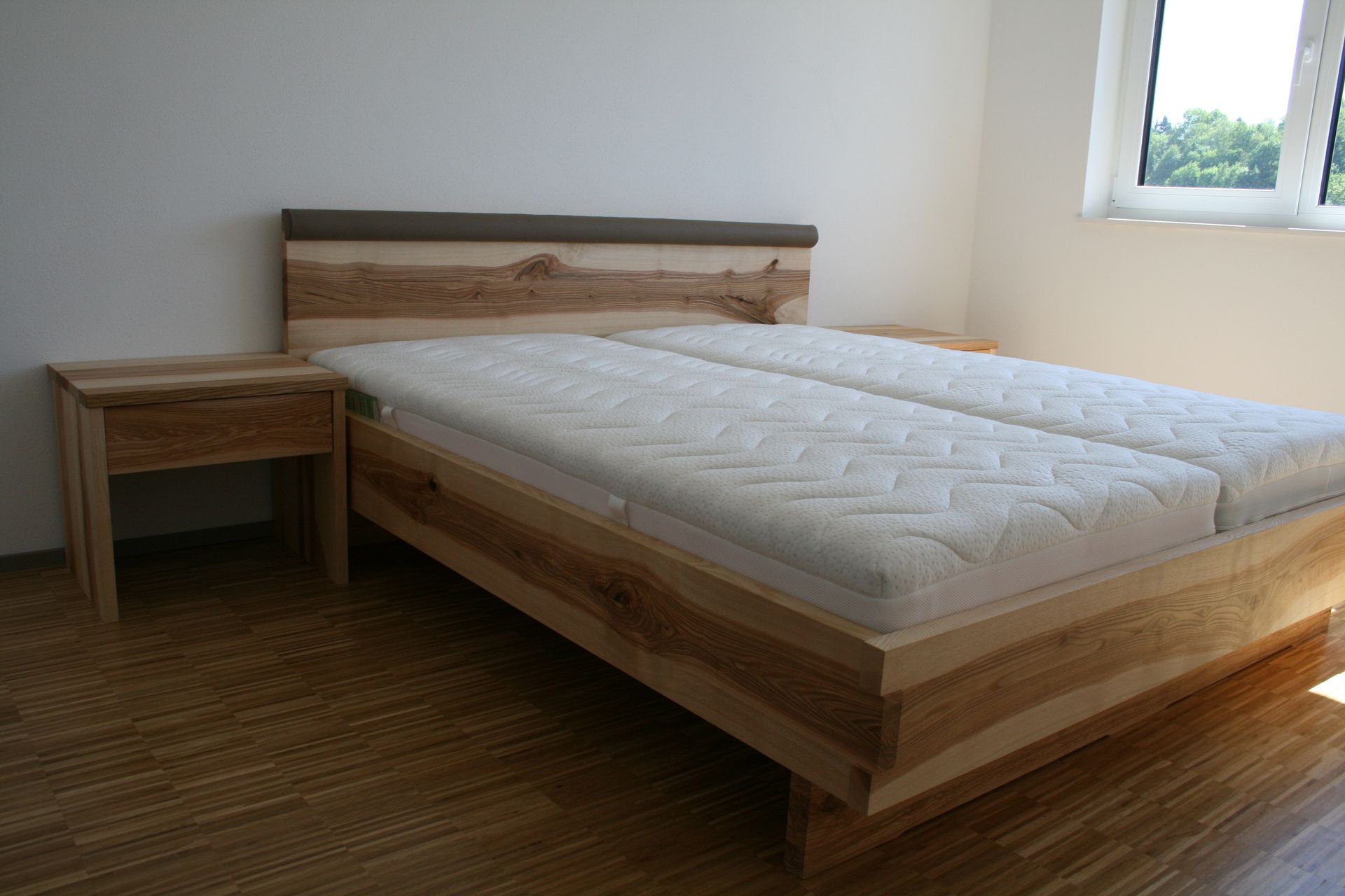 Minimalistisches Schlafzimmer mit Holzbett, Nachttisch und Fenster mit Tageslicht