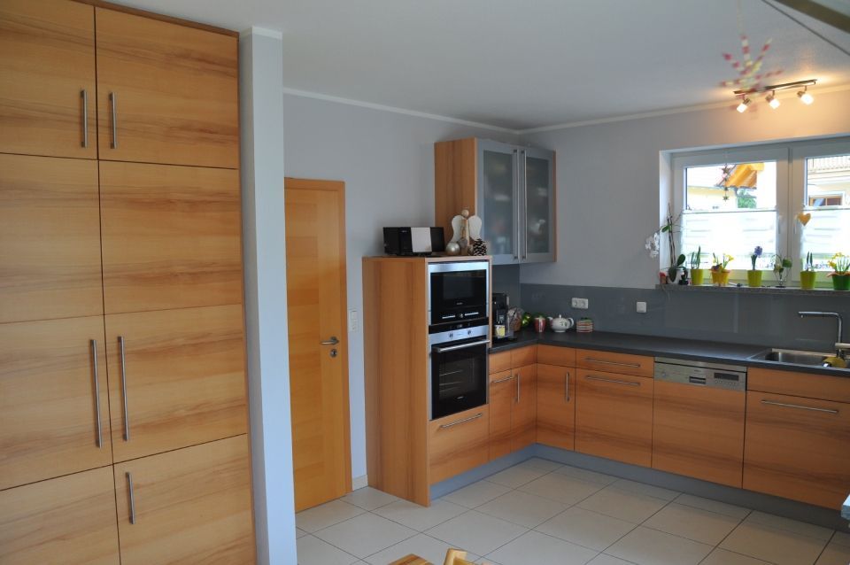Moderne Küche mit Holzschränken, Edelstahlgeräten, grauen Wänden und einem Fenster über der Spüle
