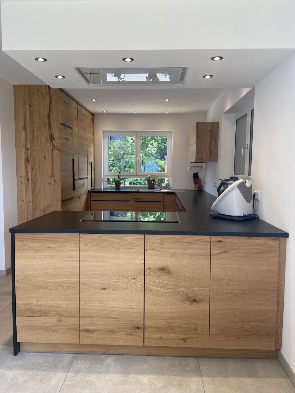 Moderne Küche mit Holzschränken, schwarzer Kücheninsel, Oberlicht und einem Fenster über der Spüle