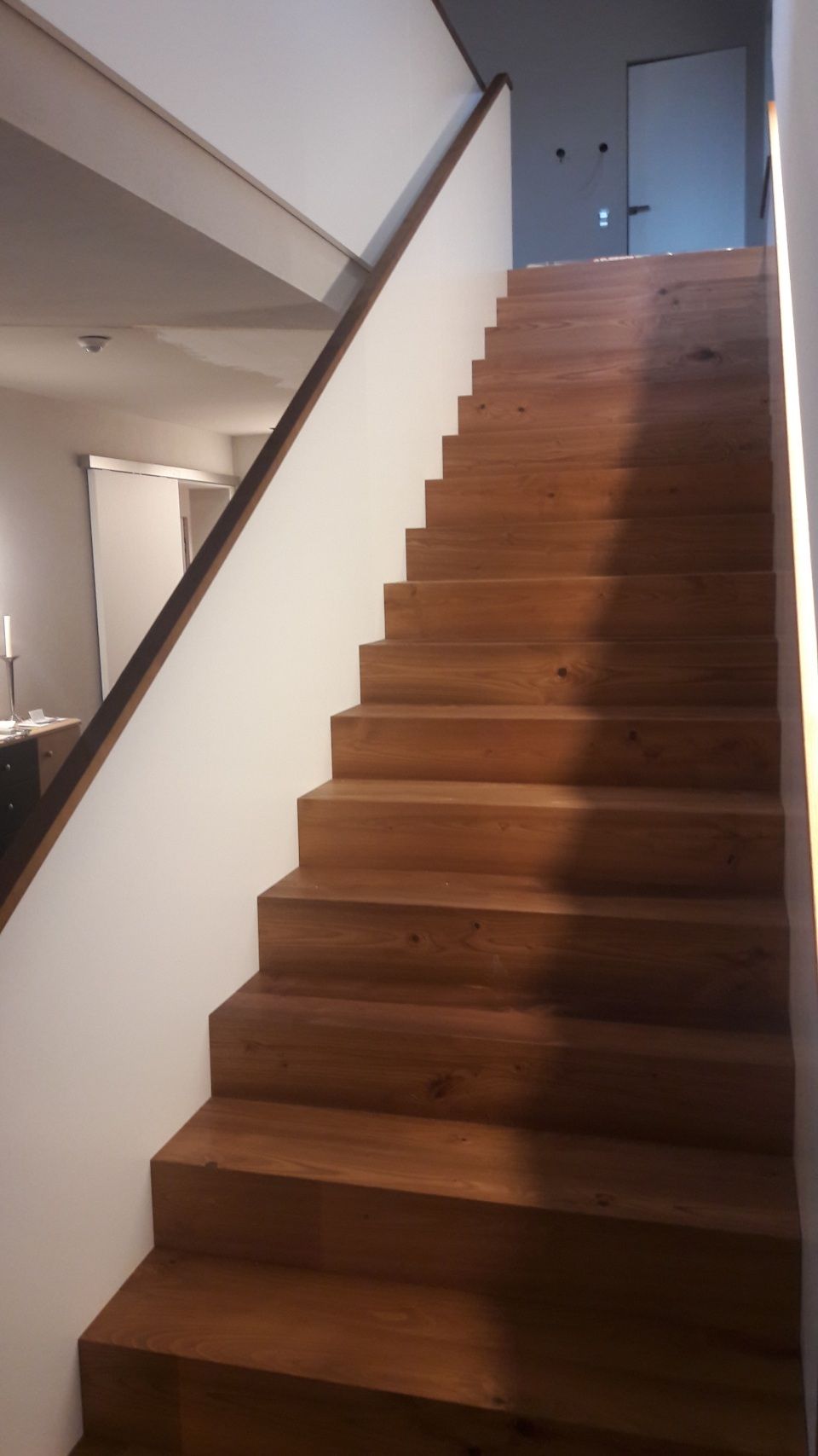 Holztreppe in einem modernen Haus mit weißen Wänden und einem Treppenabsatz oben