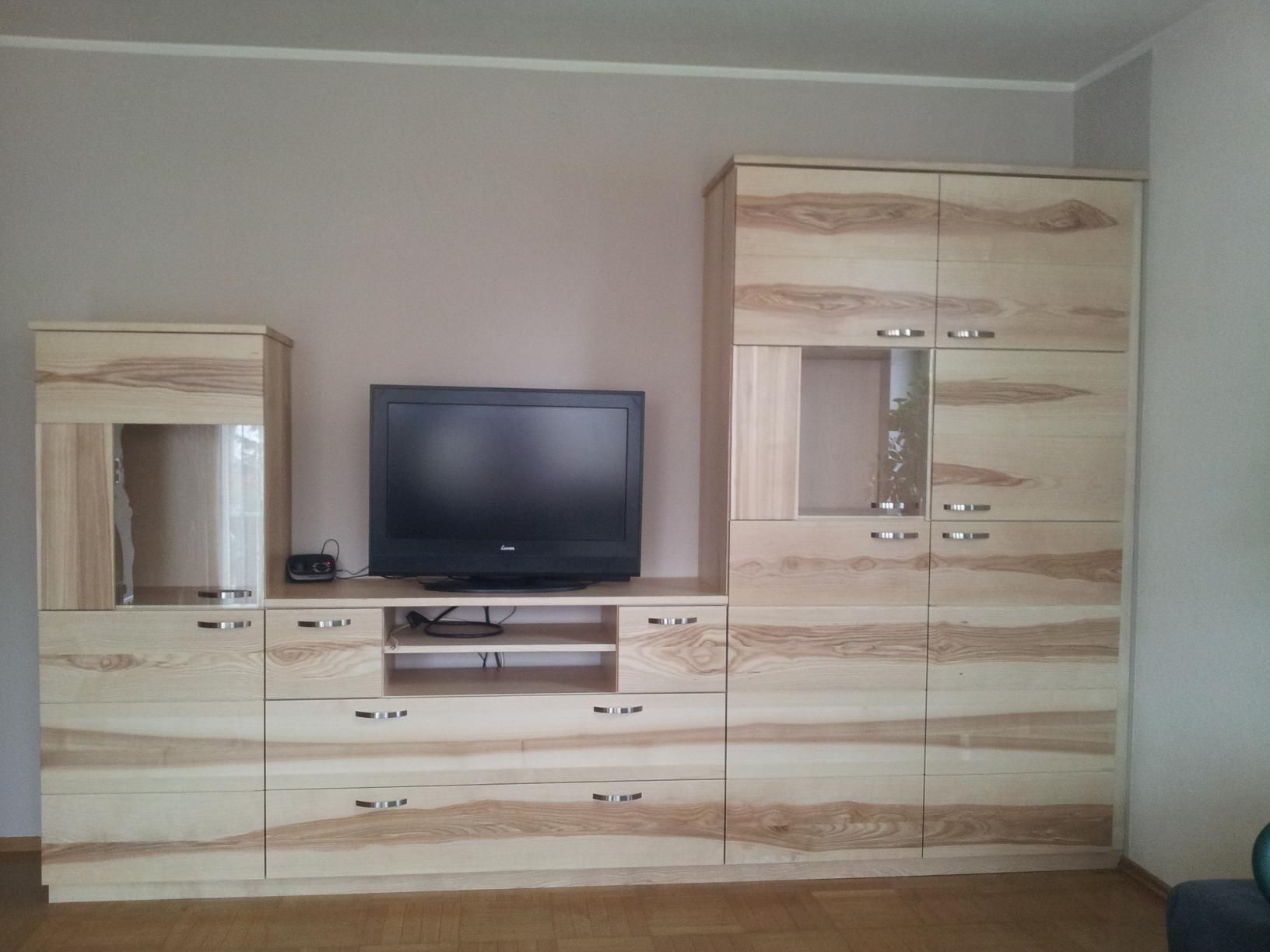 Wohnwand aus hellem Holz mit Fernseher, Schränken und Spiegel in einem spärlich möblierten Raum