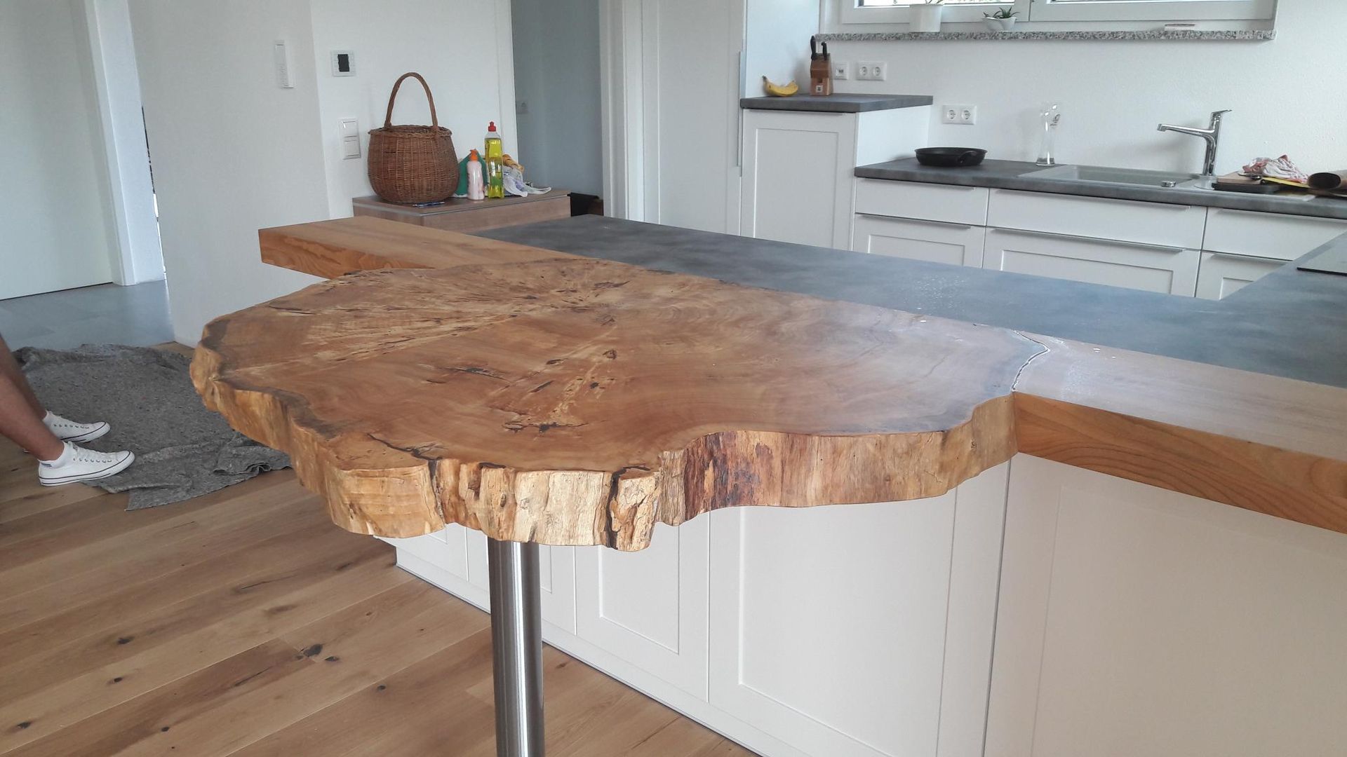 Kücheninsel aus Massivholz mit natürlicher Baumkante und Metallbeinen in einer hellen, modernen Küche