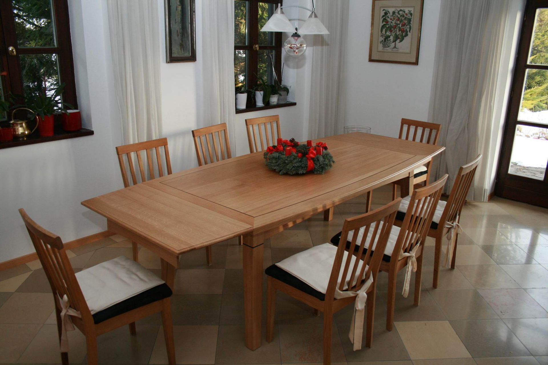 Esszimmer mit einem Holztisch und sechs Stühlen, weißen Vorhängen und einem roten Blumenarrangement als Mittelpunkt.