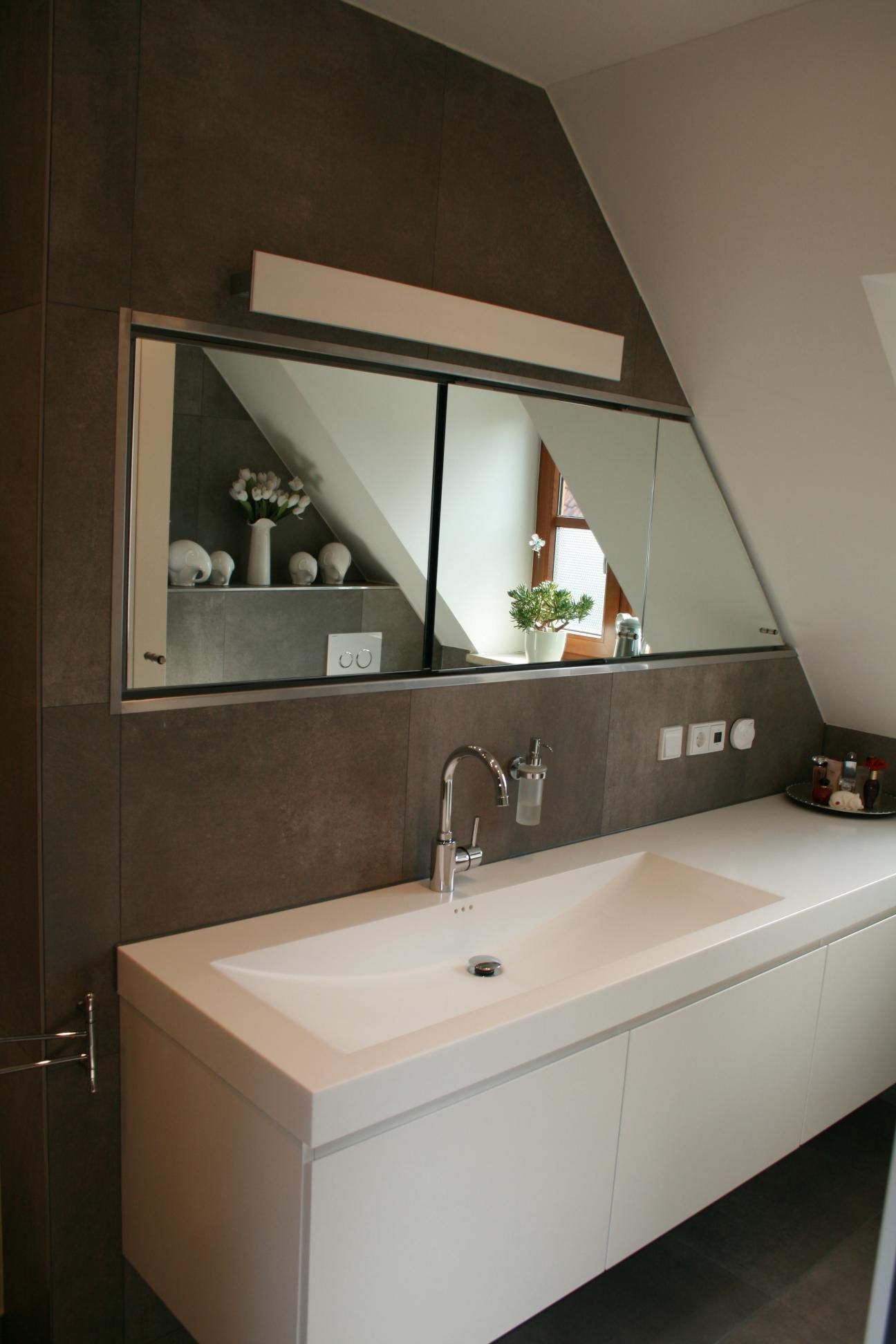 Moderner Waschtisch im Badezimmer mit weißem Waschbecken, großem Spiegel und dunkler Fliesenakzentwand