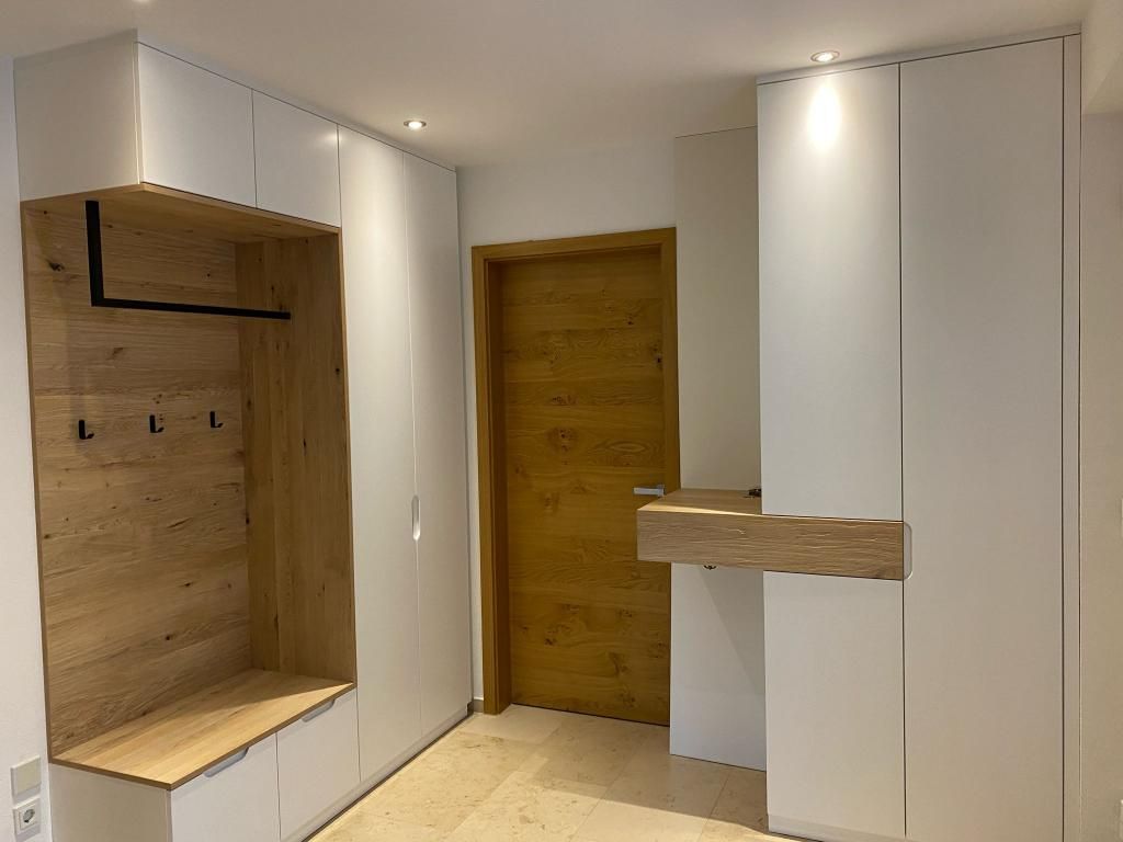Moderner Eingangsbereich mit weißen Schränken, einer Holzbank, Haken und einer Holztür