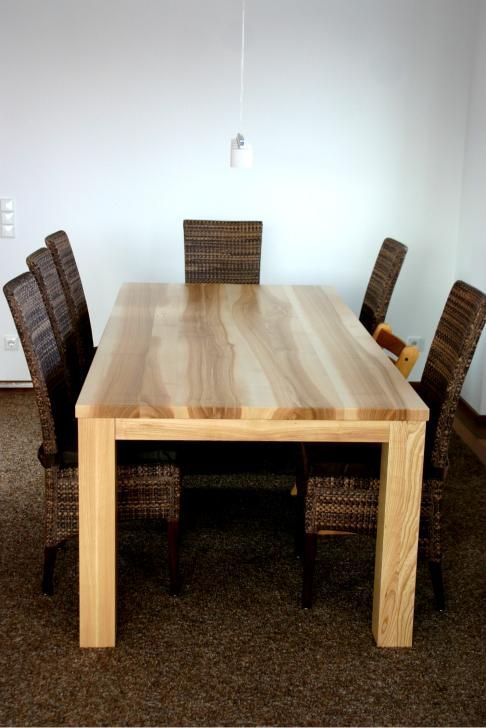 Holzesstisch mit sechs Korbstühlen in einem spärlich eingerichteten Raum vor einer weißen Wand