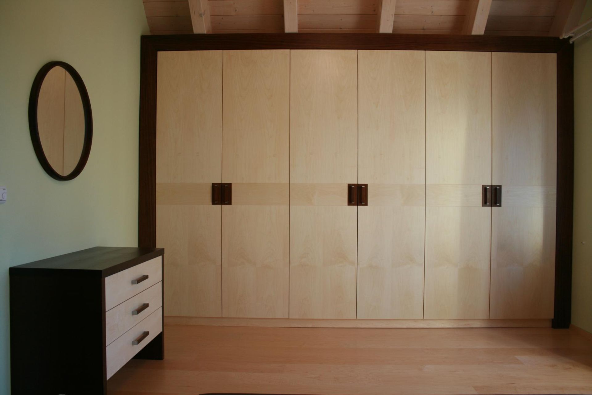 Minimalistisches Schlafzimmer mit großem Einbauschrank aus Holz, Kommode und ovalem Wandspiegel