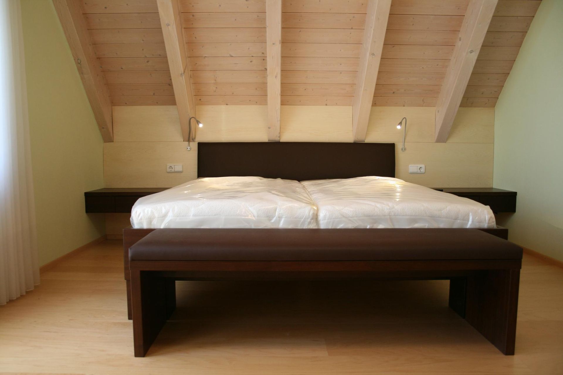 Minimalistisches Schlafzimmer mit einem Bett aus dunklem Holz unter einer schrägen Holzdecke