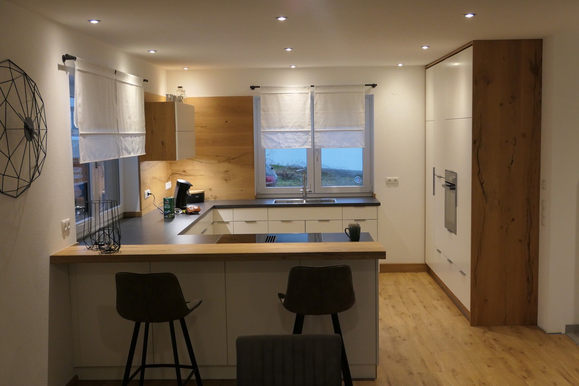 Moderne Küche mit weißen Schränken, Holzakzenten, Hockern an der Kücheninsel und einem Fenster mit Blick aufs Wasser.