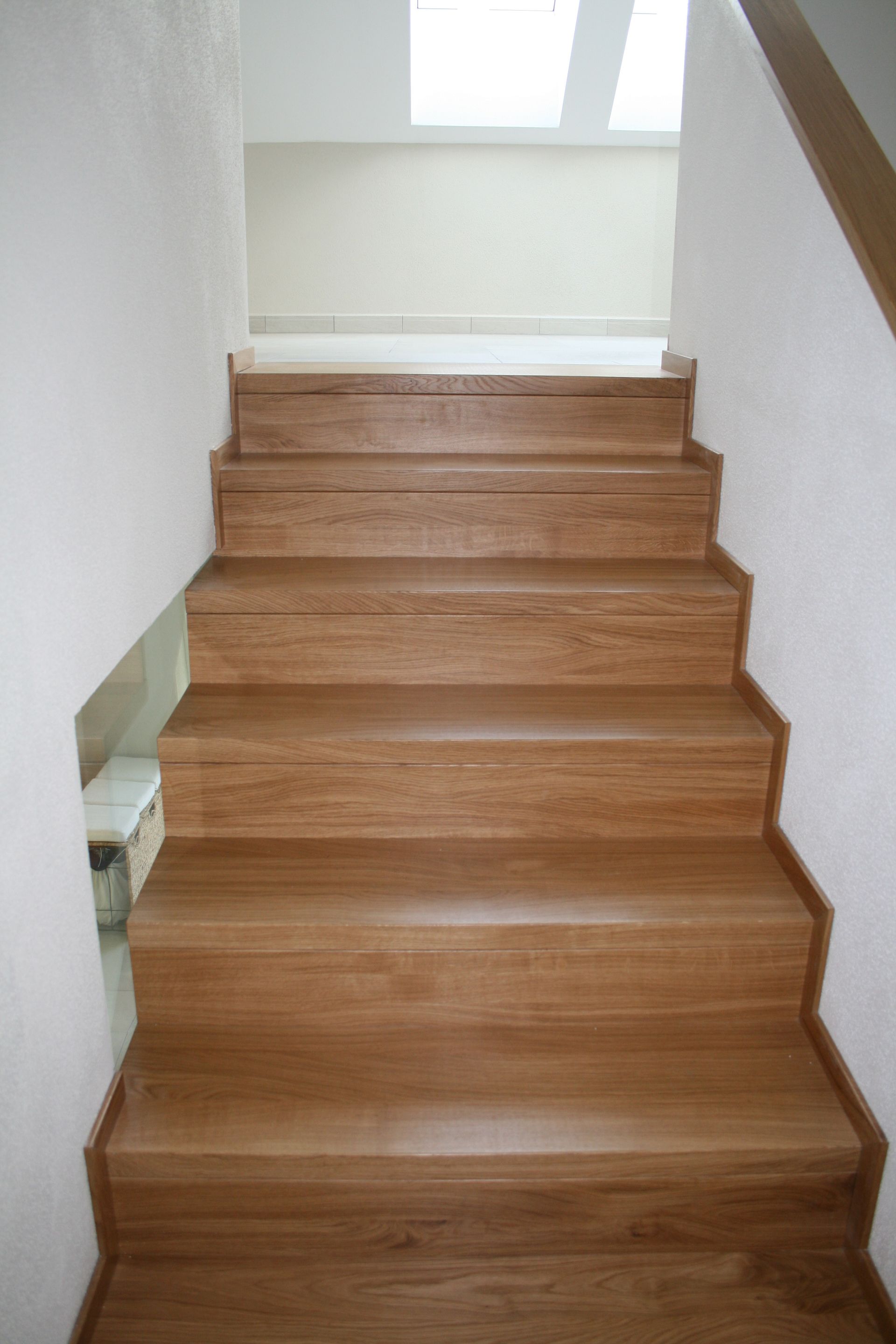 Holztreppe mit weißen Wänden und einem Oberlicht darüber, von unten gesehen.