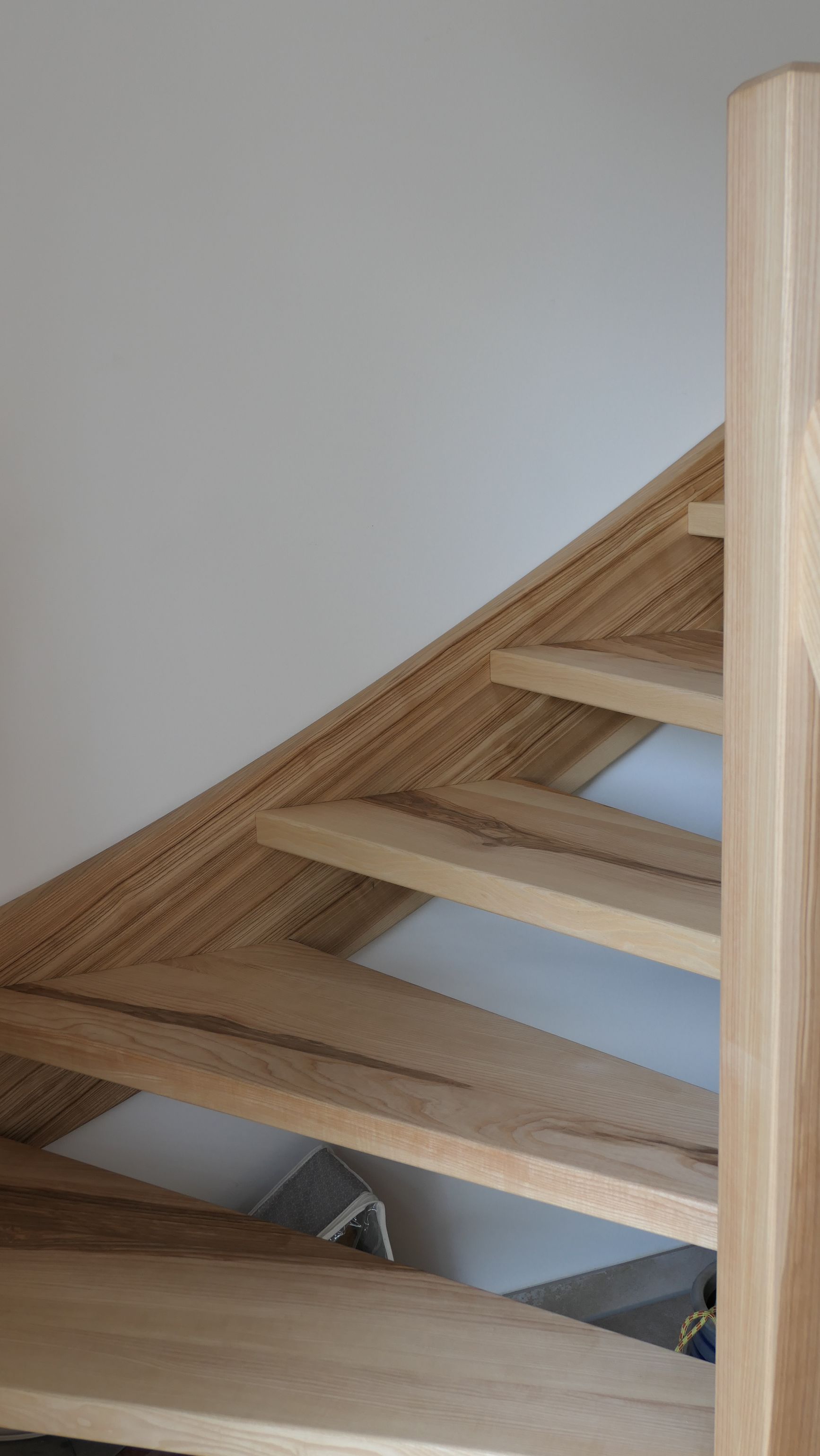 Holztreppe mit offenen Setzstufen und hellem Holzgeländer vor einer schlichten weißen Wand