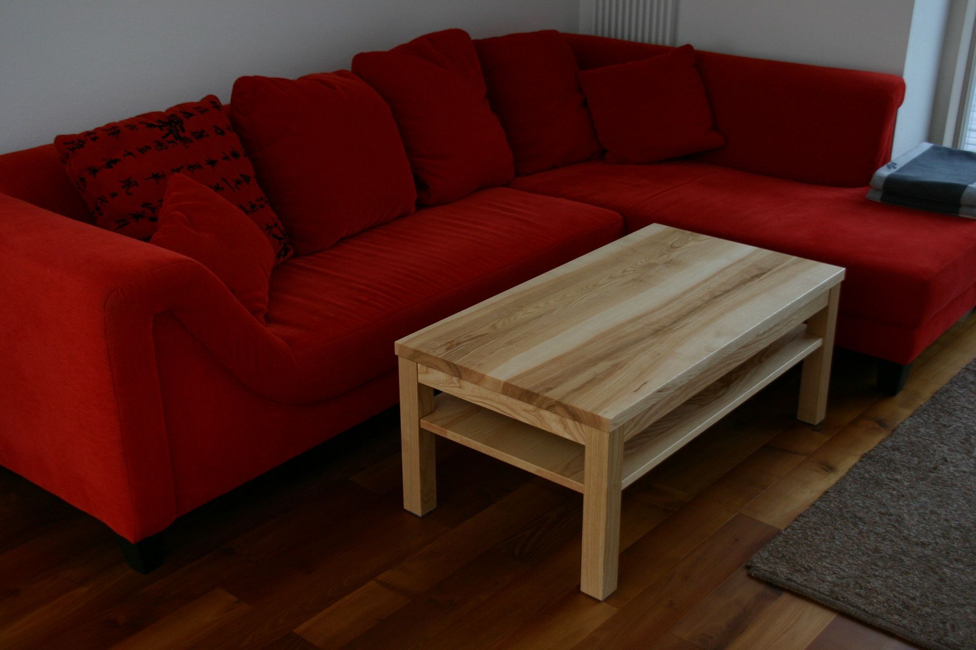 Rotes Ecksofa mit Kissen und ein heller Couchtisch aus Holz auf einem Parkettboden.