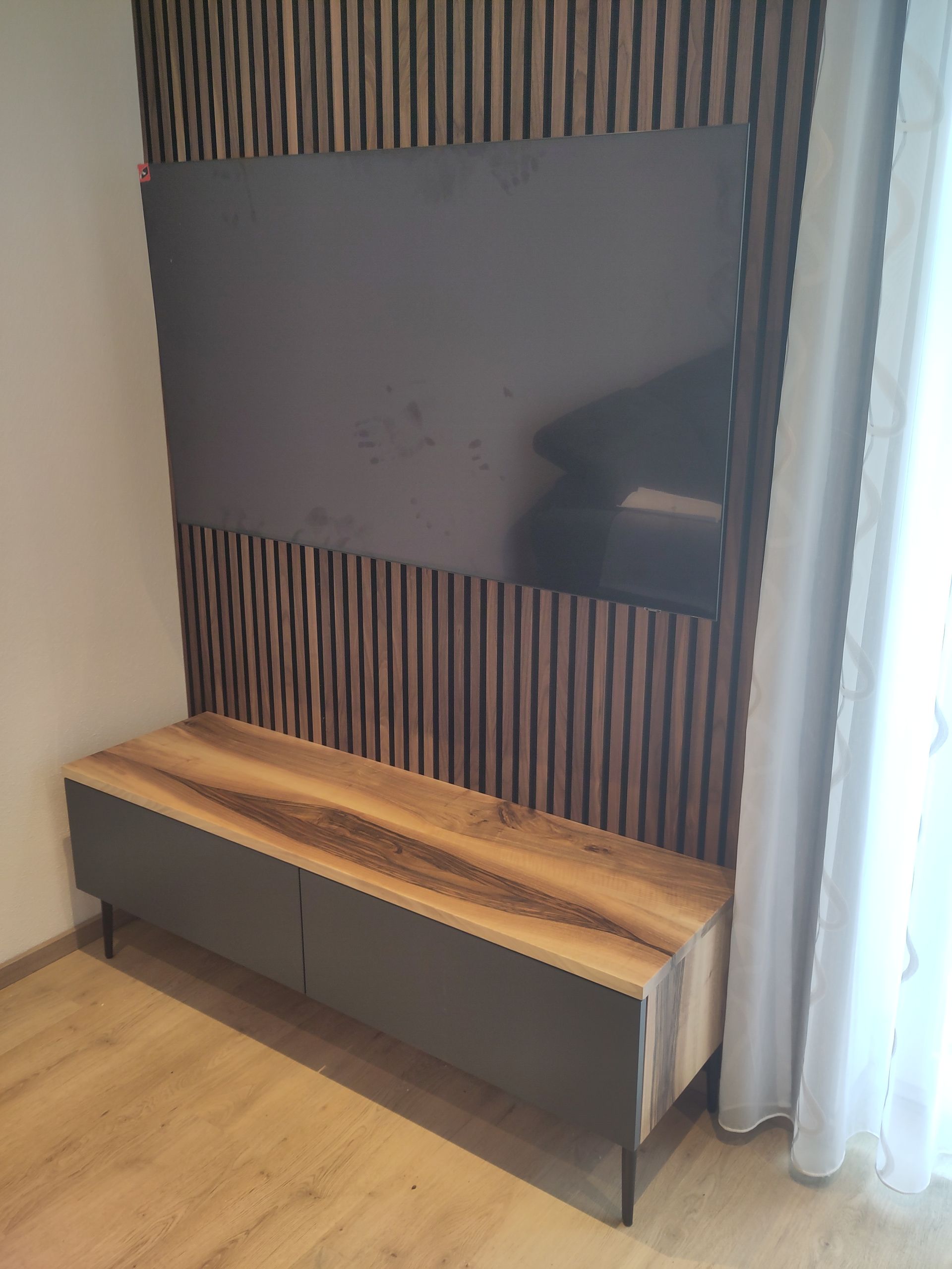 Moderne Sitzbank im Eingangsbereich mit Holzlatten, dunklen Schränken und einem großen Spiegel neben transparenten Vorhängen.