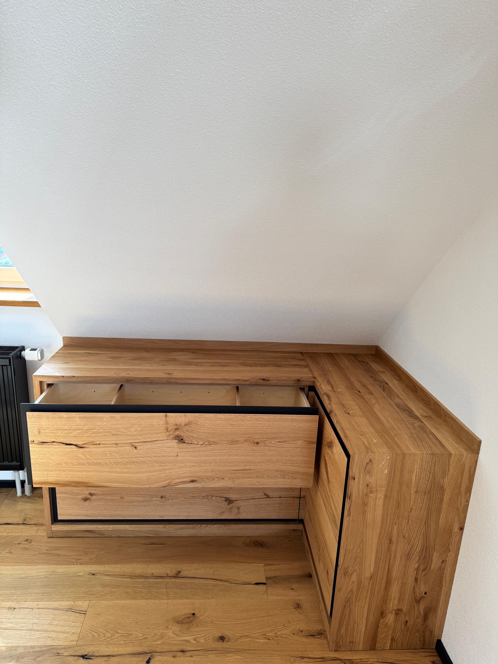 L-förmiger Holzschreibtisch mit einer offenen Schublade in einer Ecke vor weißen Wänden.