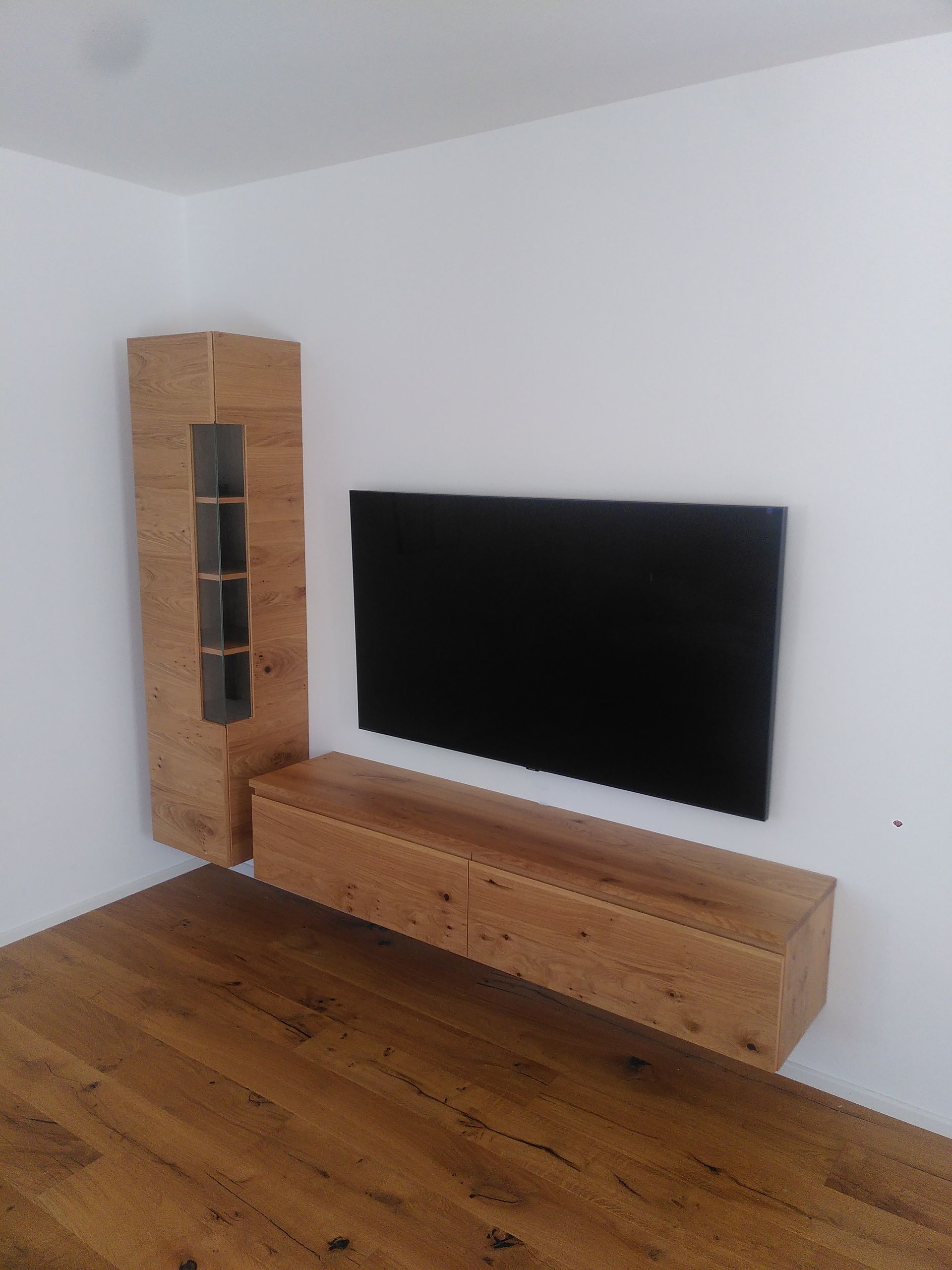 Modernes Wohnzimmer mit wandmontiertem Fernseher, TV-Lowboard aus Holz und hohem Schrank auf einem Hartholzboden