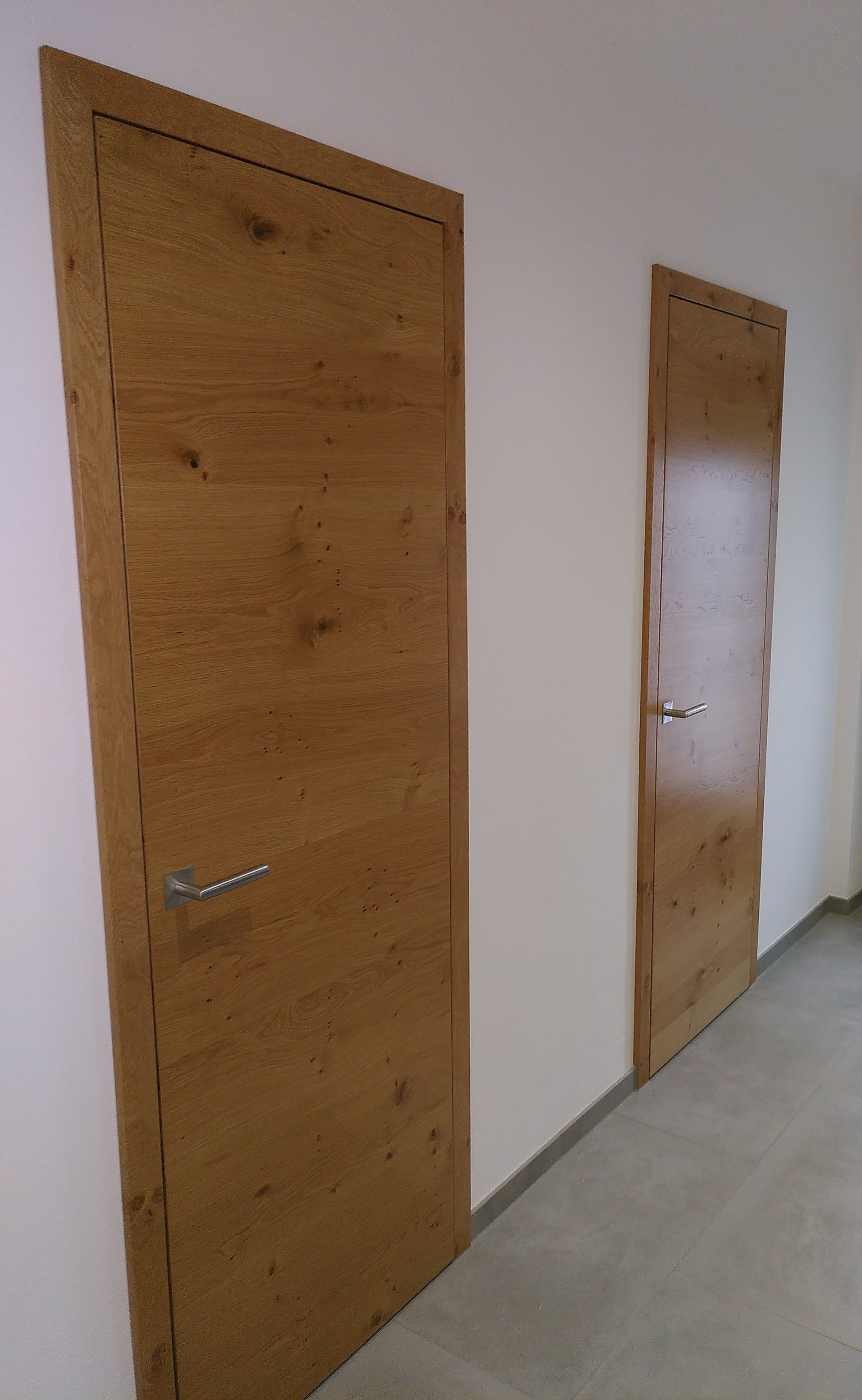 Zwei Holztüren in einem schlichten Flur, eine große im Vordergrund und eine kleinere in der Ferne.