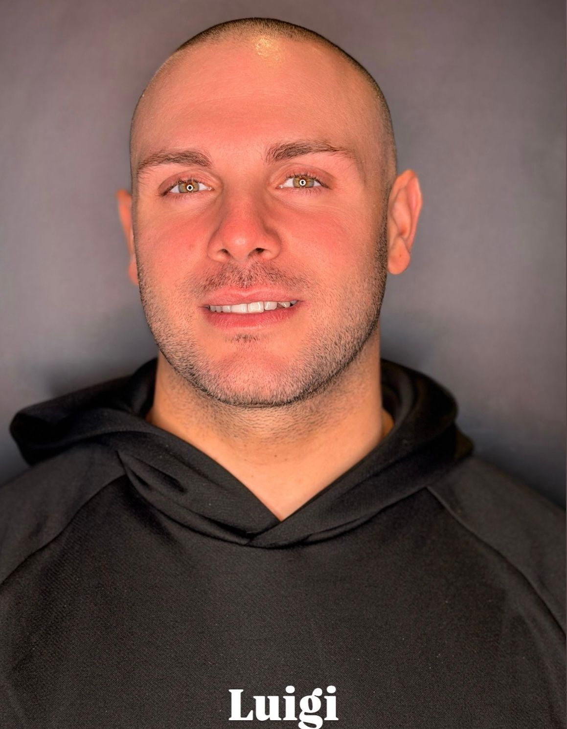 Un primo piano di Luigi che indossa una felpa nera con cappuccio su uno sfondo grigio.
