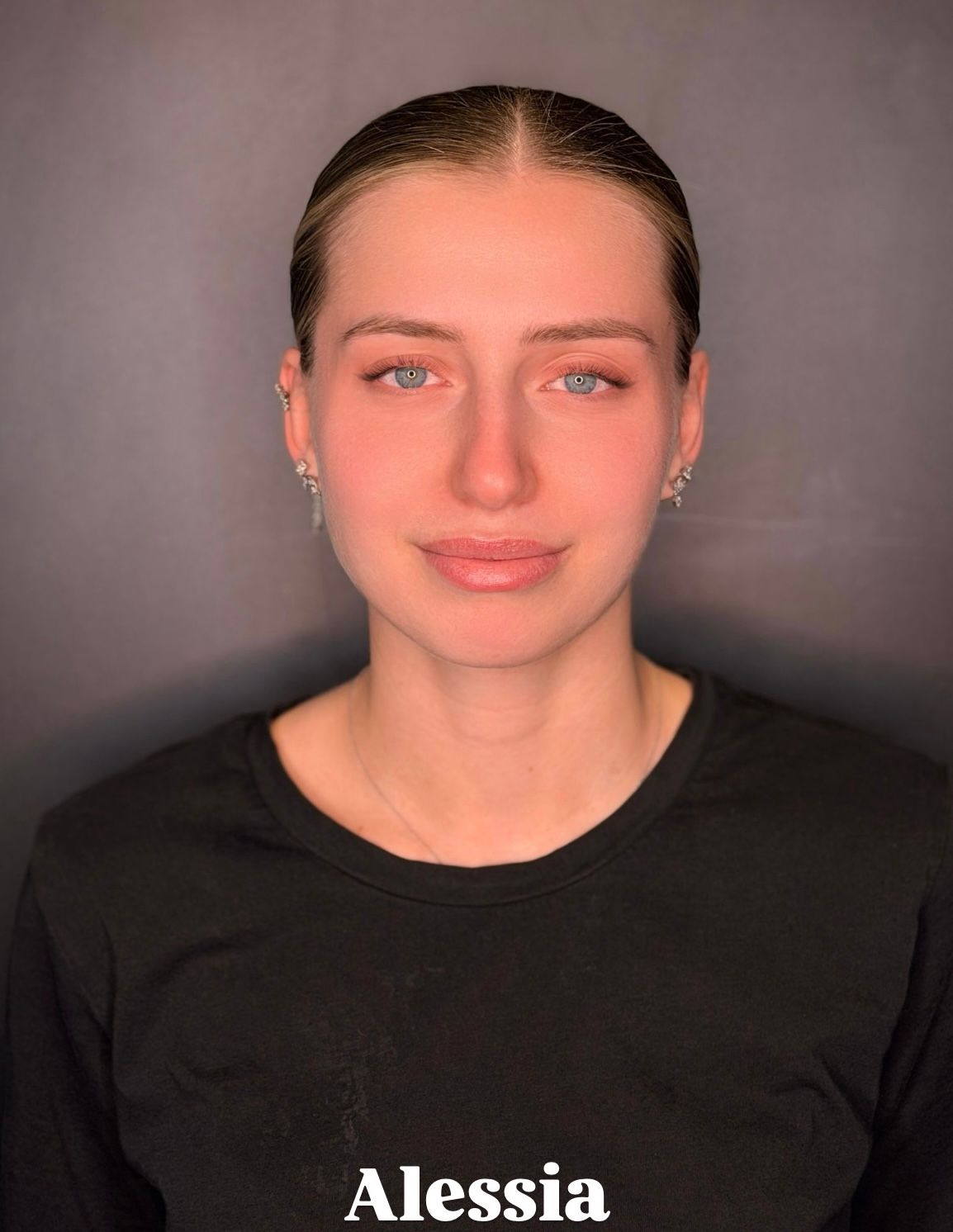 Alessia, con i capelli castani raccolti, indossa una camicia nera su uno sfondo scuro e guarda direttamente in camera.