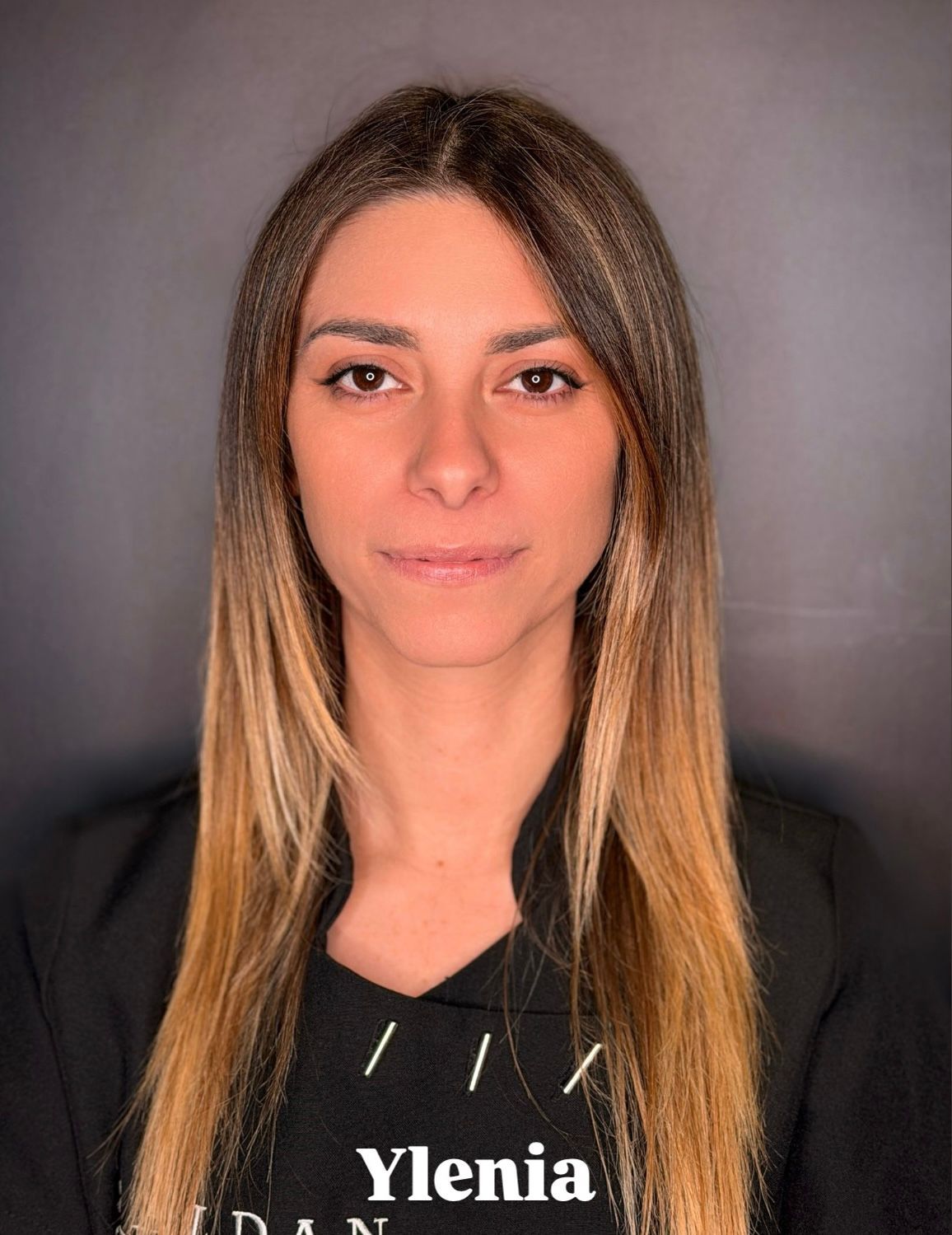 Ritratto di una persona con lunghi capelli bicolore che indossa una camicia nera su uno sfondo grigio scuro uniforme.