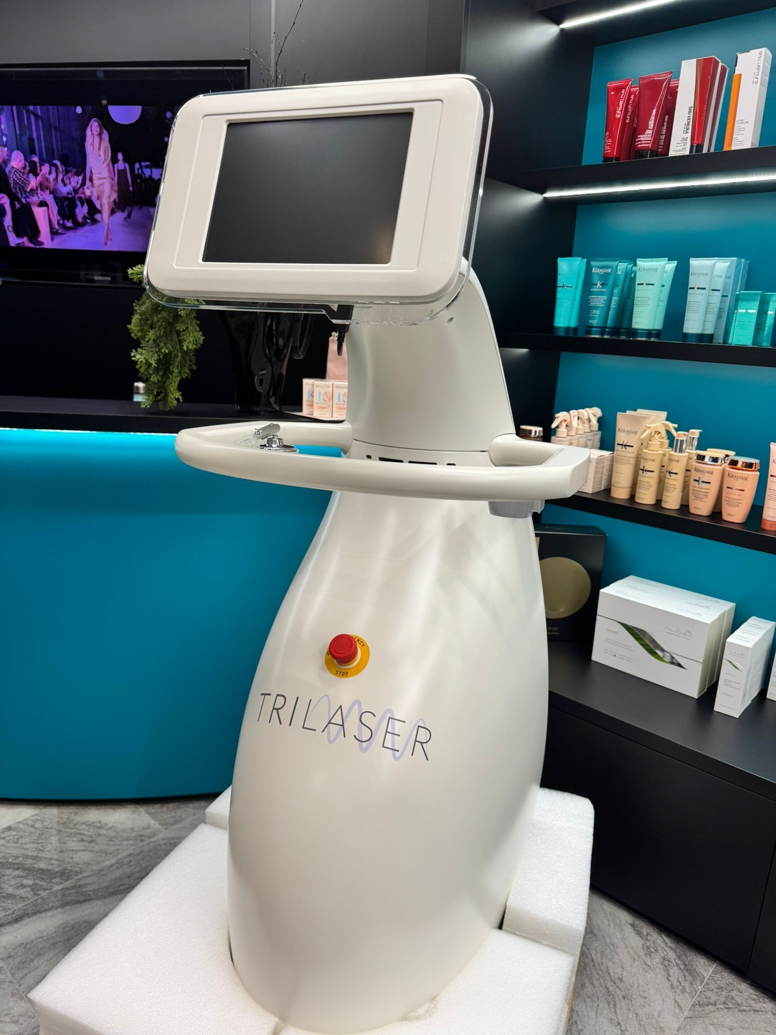 Un apparecchio bianco, dal design moderno, con schermo touchscreen e pulsante di arresto di emergenza, collocato in un salone di bellezza.
