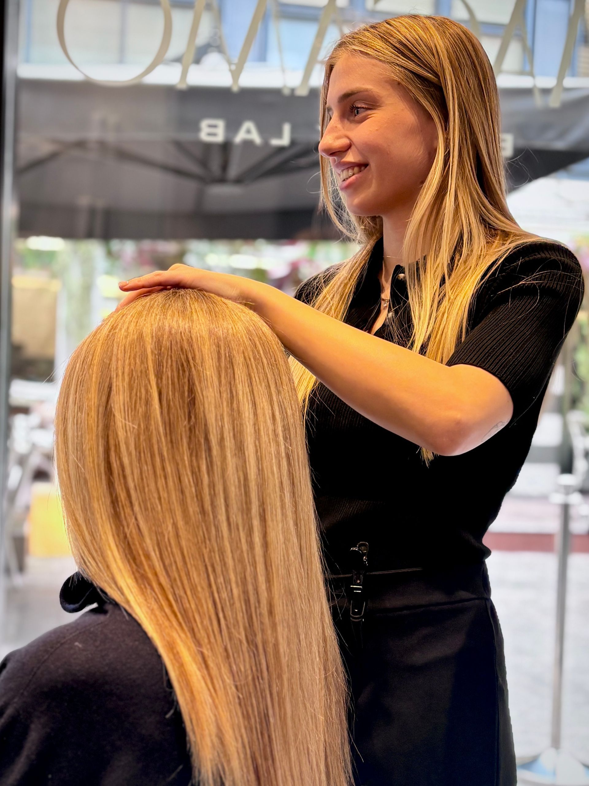 In un salone, una parrucchiera con i capelli biondi intrecciati acconcia i lunghi capelli biondi e lisci di una cliente.
