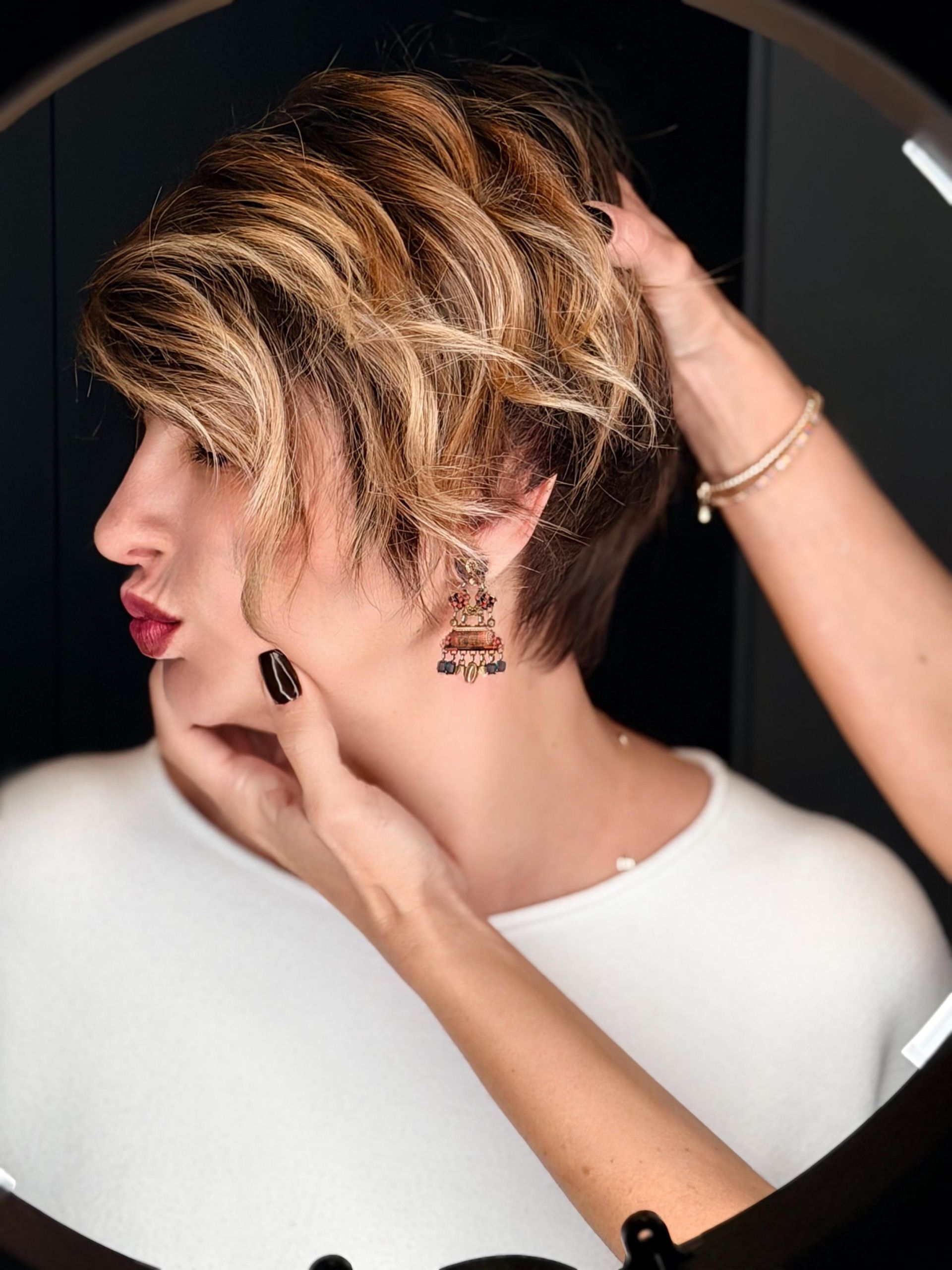 Una persona con i capelli corti e biondi con ciocche posa con le labbra serrate, mentre una mano le tocca la guancia e le sistema i capelli.