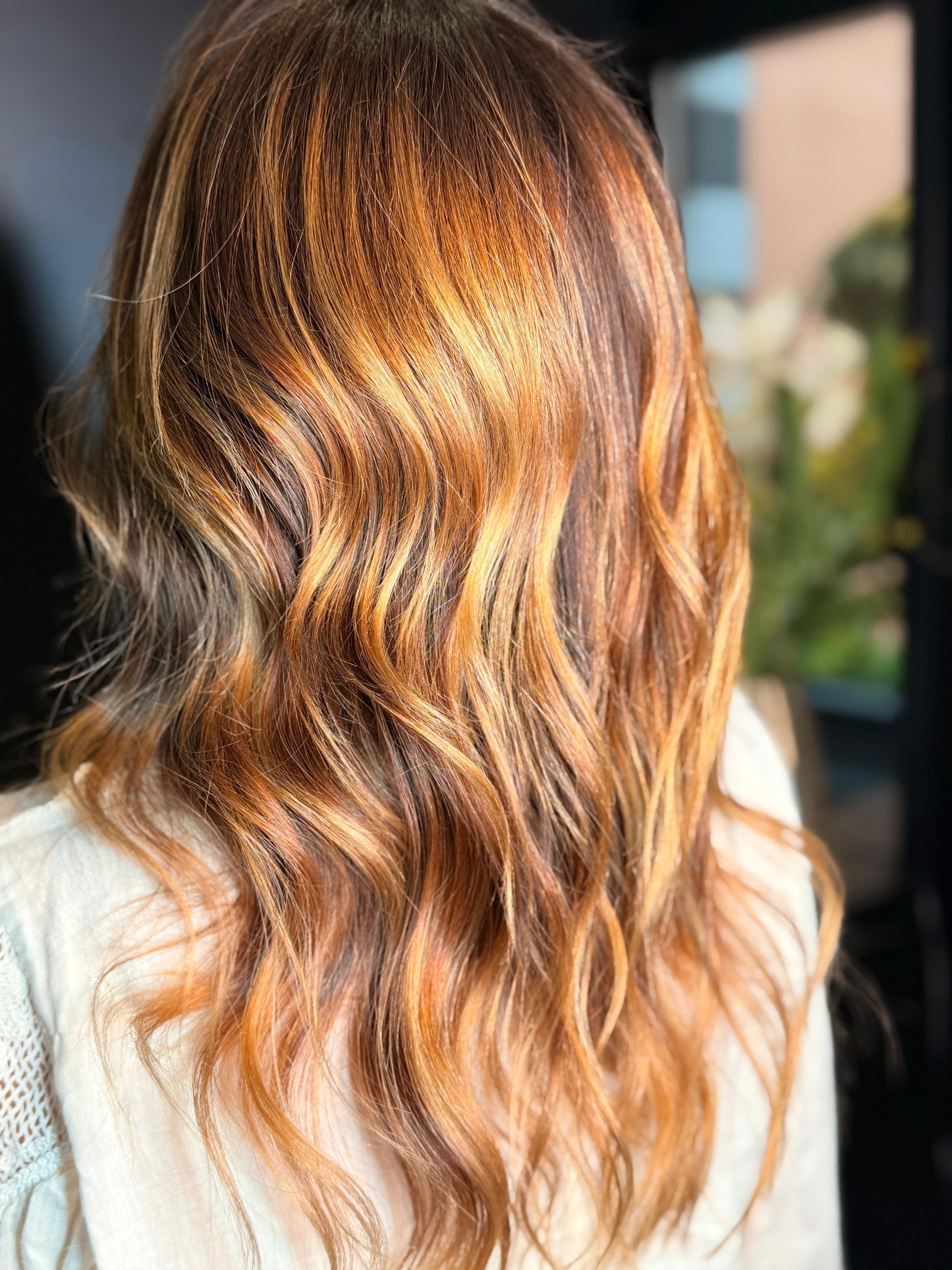 Capelli di media lunghezza, acconciati in morbide onde, con riflessi castano caldo e biondo dorato.