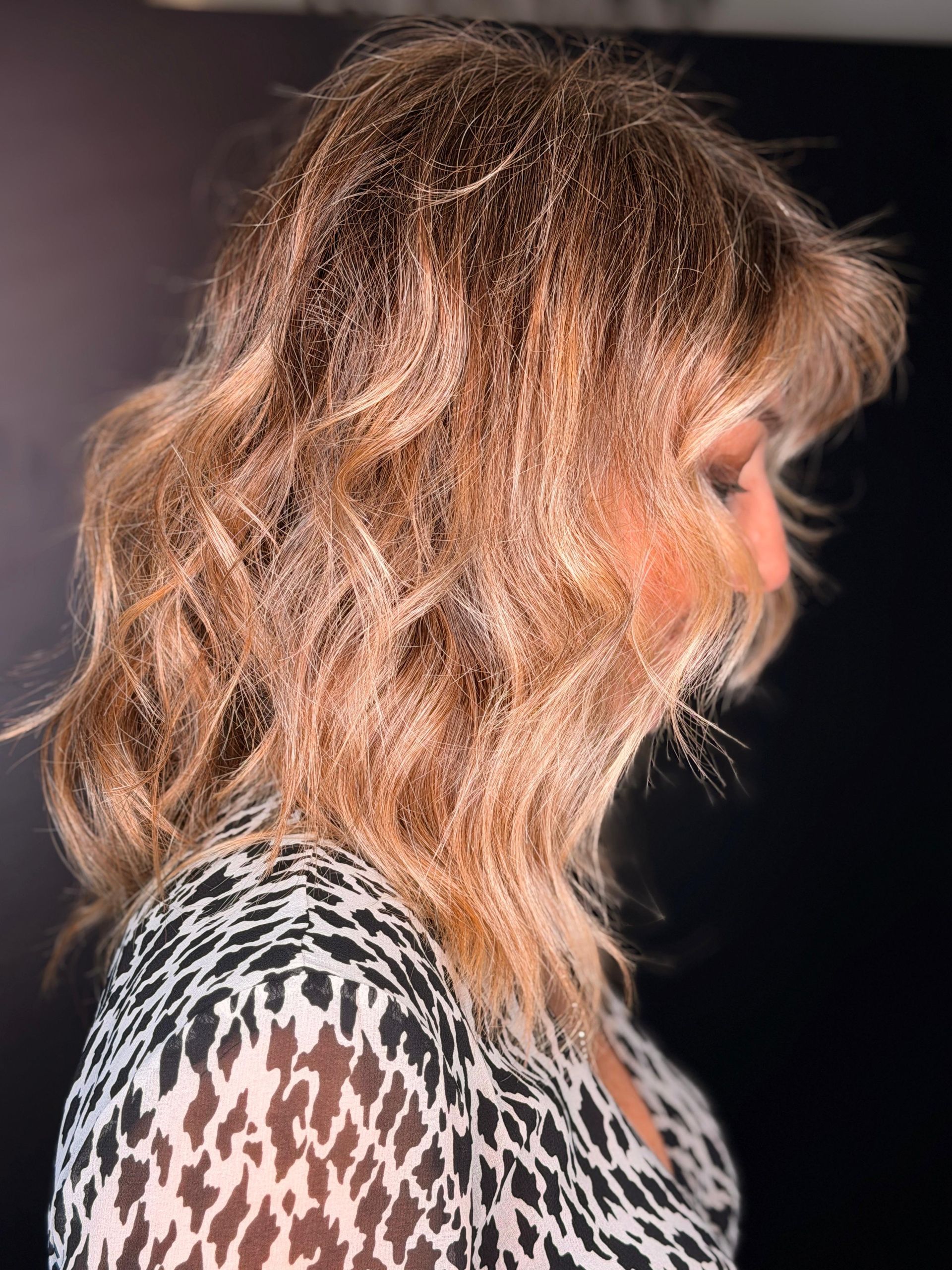 Vista di profilo di una persona con capelli biondi ondulati di media lunghezza che indossa una maglietta a fantasia bianca e nera.