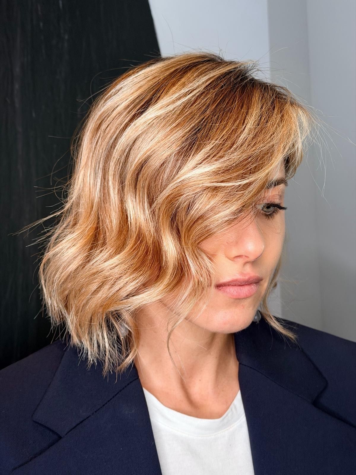 Una persona con capelli biondi, mossi e con mèches, lunghi fino al mento, che indossa un blazer blu scuro e una camicia bianca, su uno sfondo neutro. MAGAMO Lugano