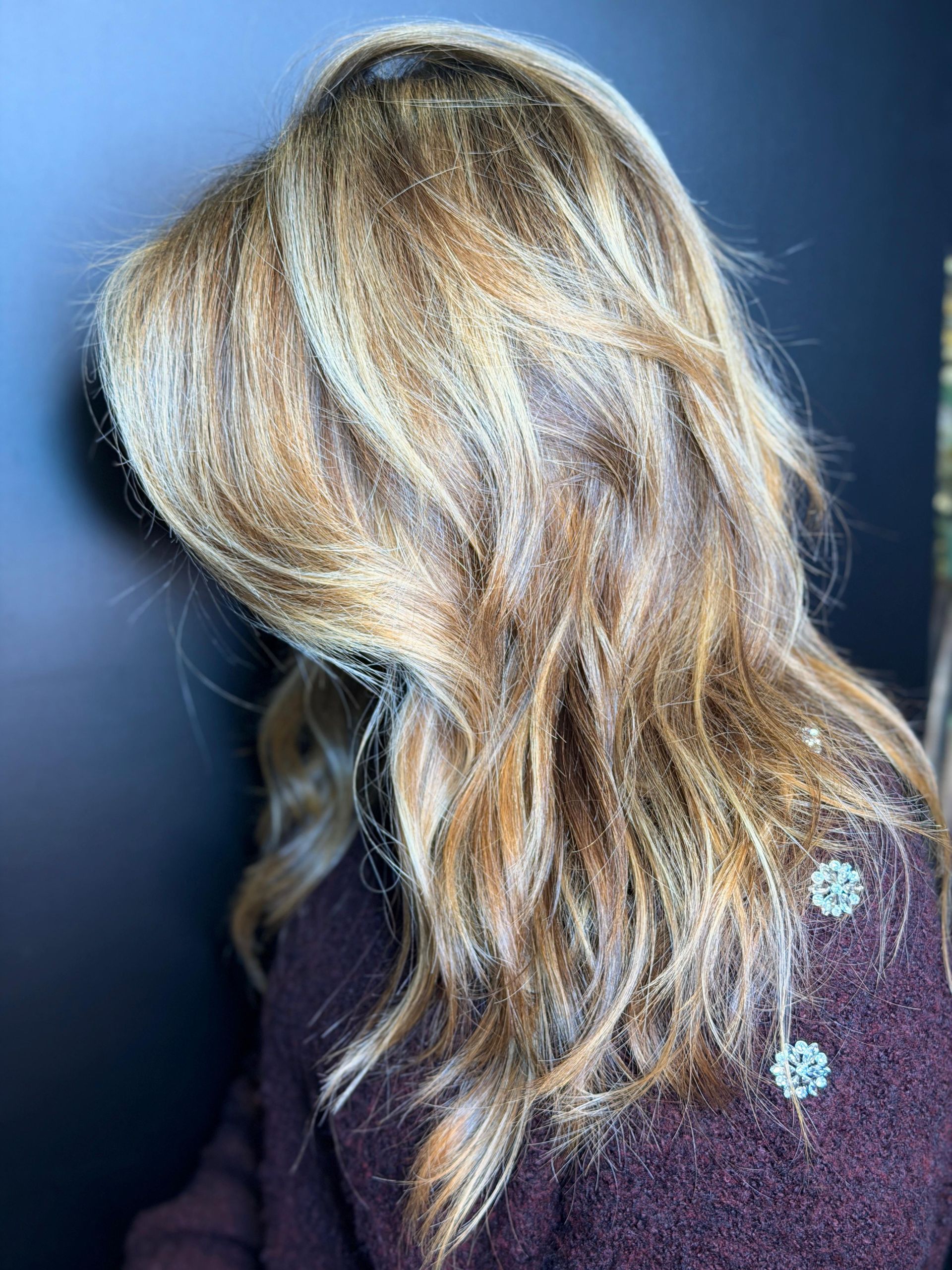 Primo piano di capelli con riflessi biondi e castano chiaro, acconciati in morbide onde texturizzate su uno sfondo scuro.