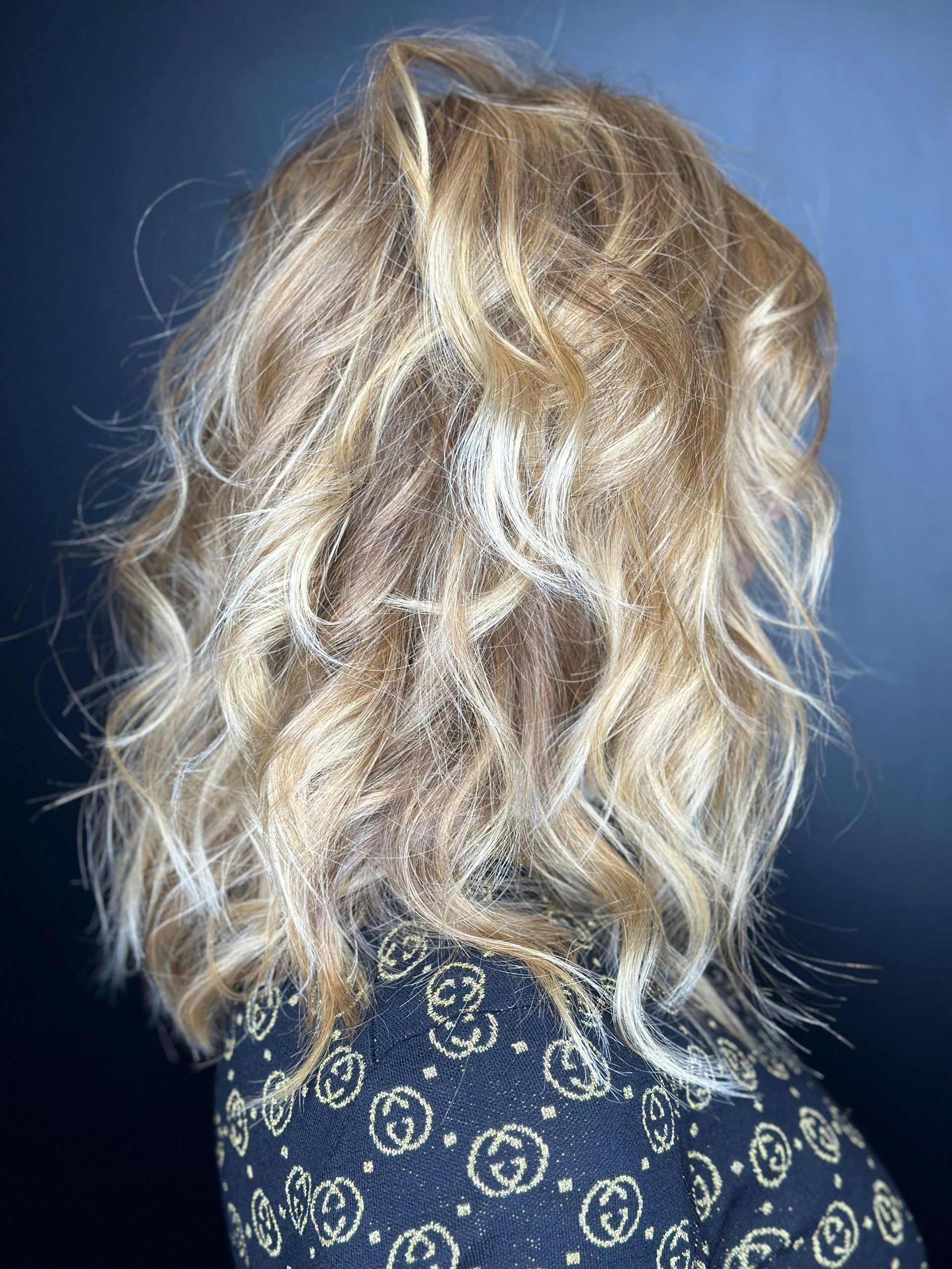 Una persona con capelli biondi ondulati, lunghi fino alle spalle, portati sciolti, su uno sfondo blu uniforme. MAGAMO Lugano