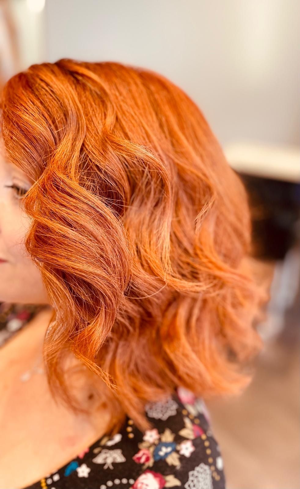 Profilo laterale di una persona con capelli mossi, di un vivace color zenzero, portati all'altezza delle spalle.