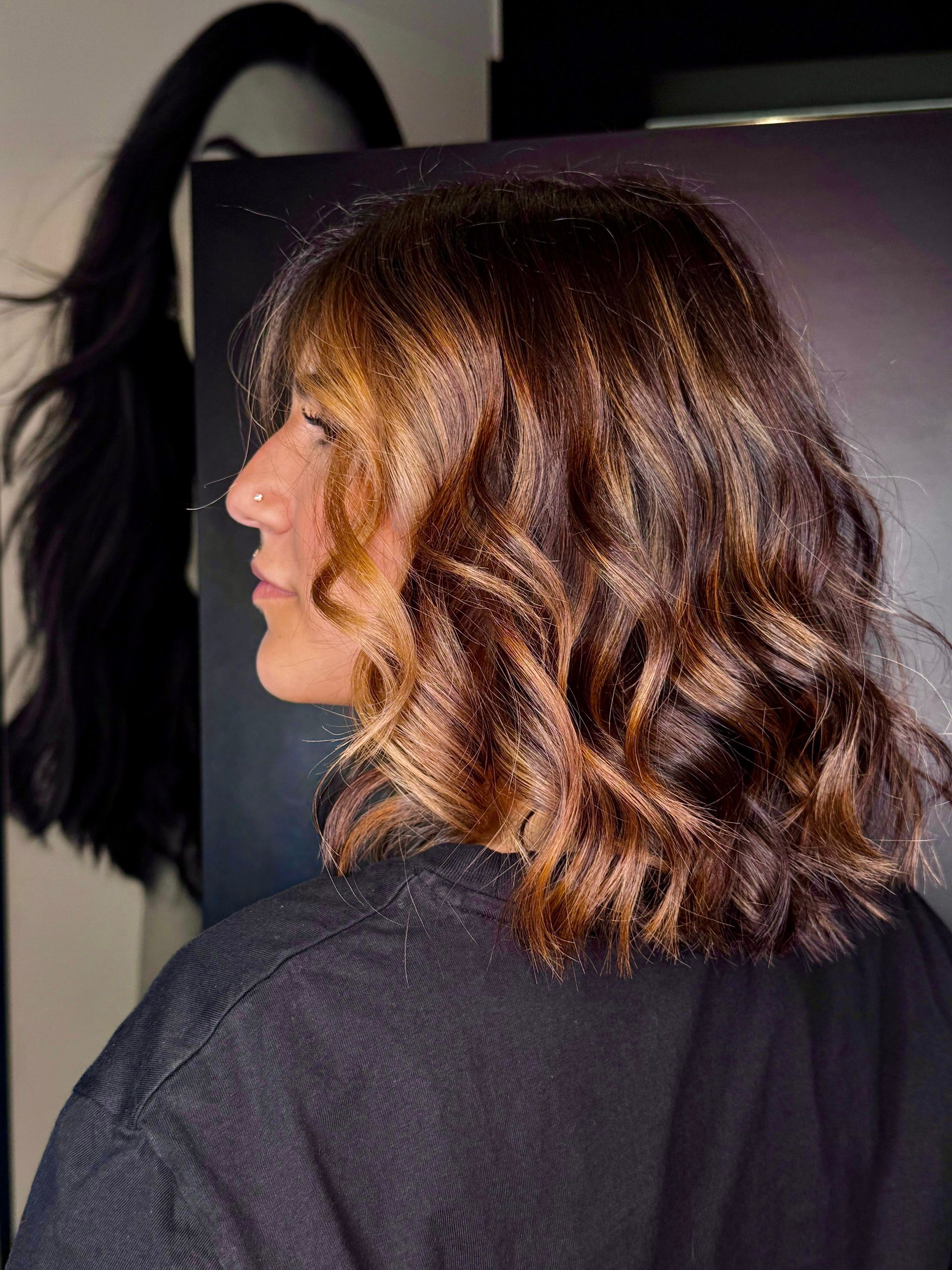 Profilo laterale di una persona con capelli castani, mossi e lunghi fino alle spalle, con mèches, che indossa una camicia nera.
MAGAMO Lugano